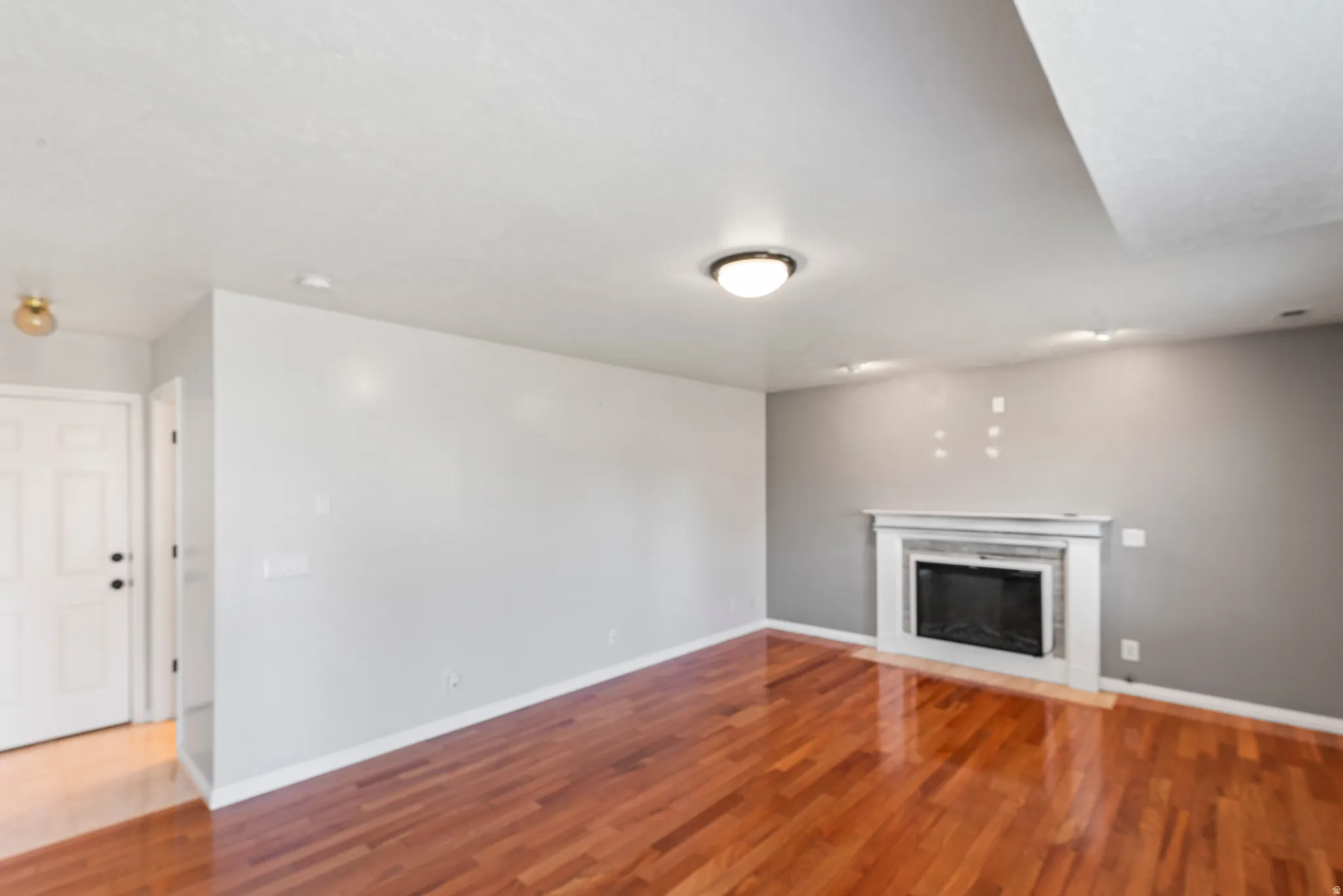 Living area featuring wood-finish flooring, a white mantelpiece, a dark-colored fireplace insert, and neutral wall paint