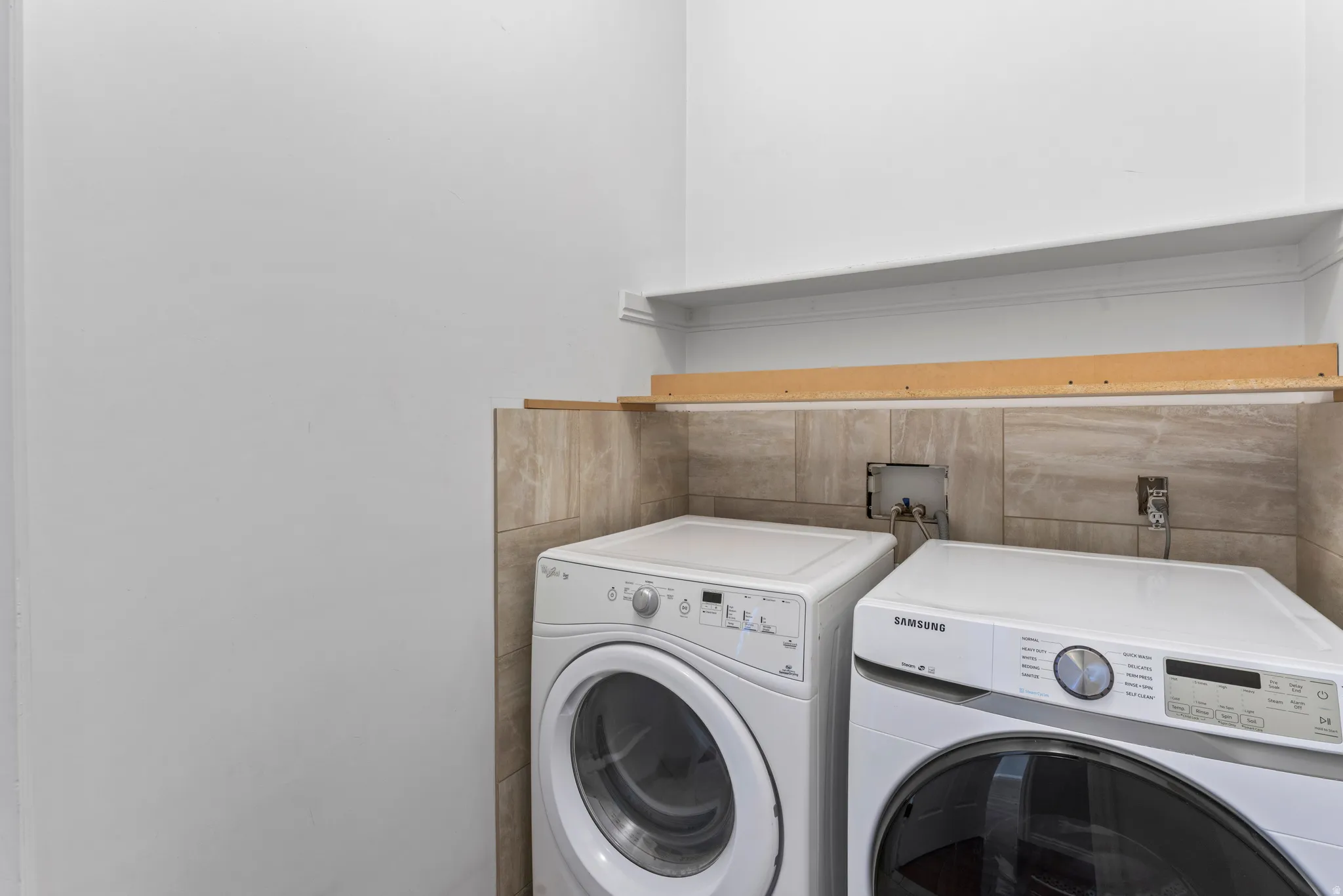 Dedicated laundry area featuring wall tiling, white walls, and a wall-mounted shelf