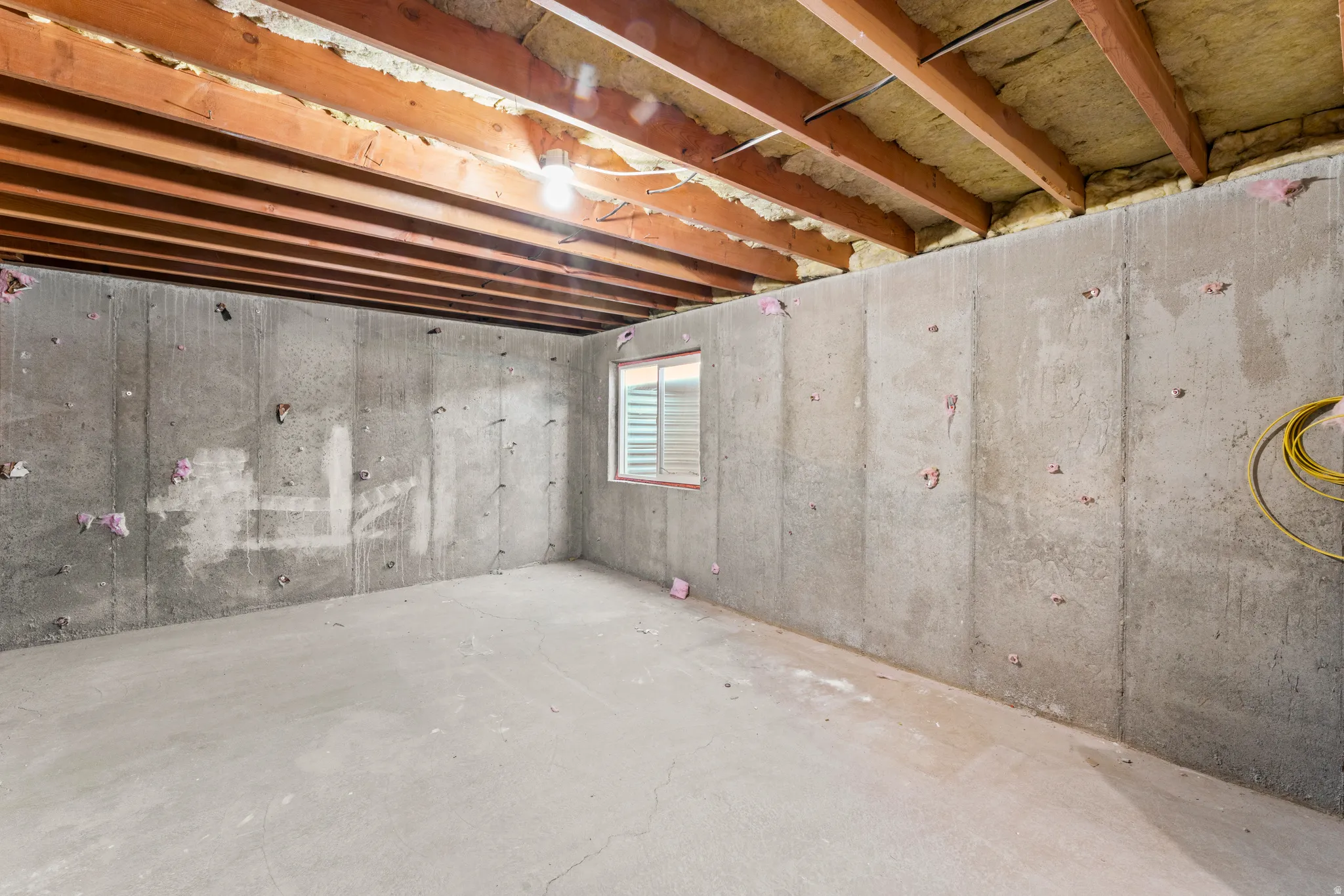 Unfinished basement space featuring exposed wood joists and concrete walls