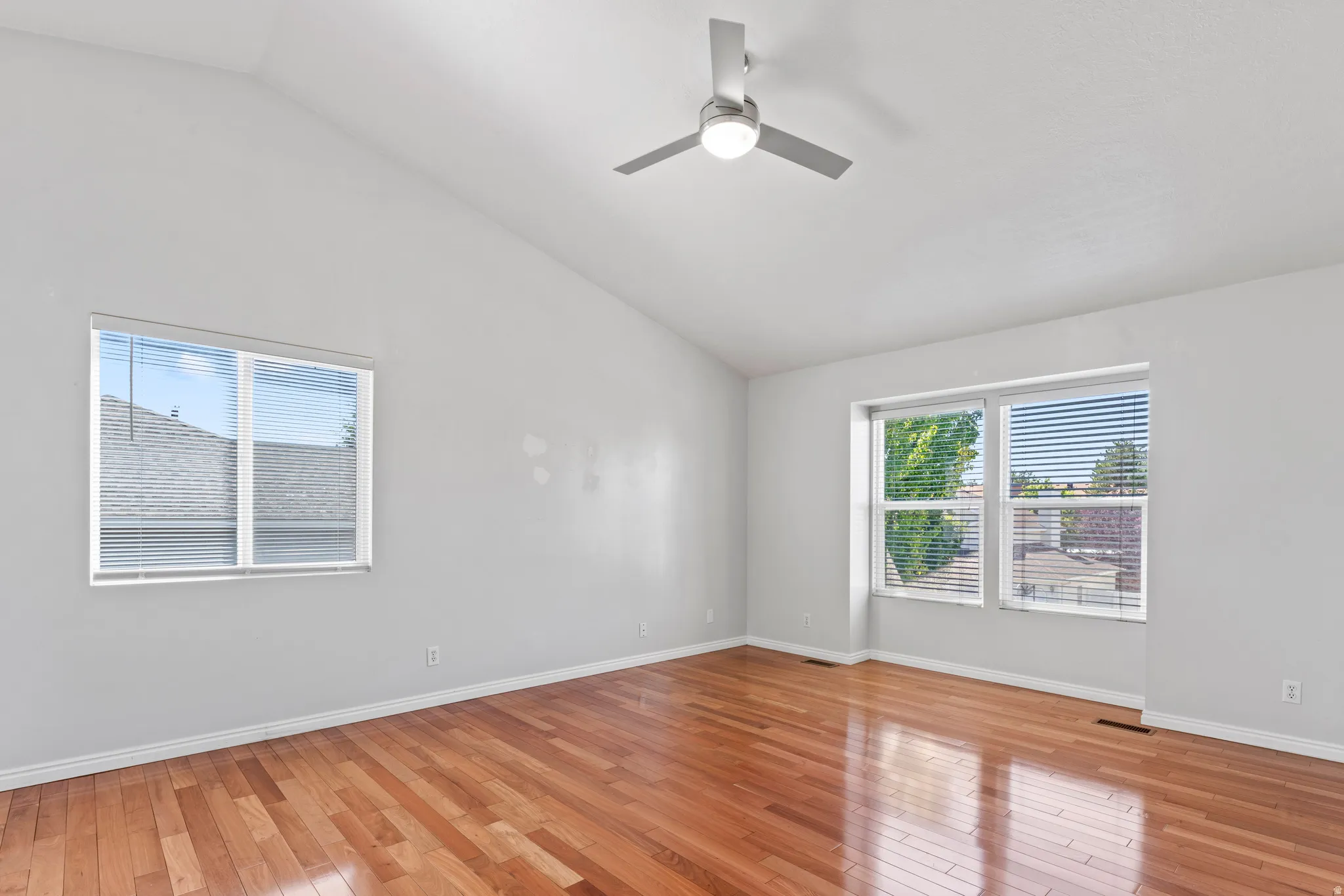 Spacious room featuring vaulted ceilings, wood-finish flooring, and multiple windows