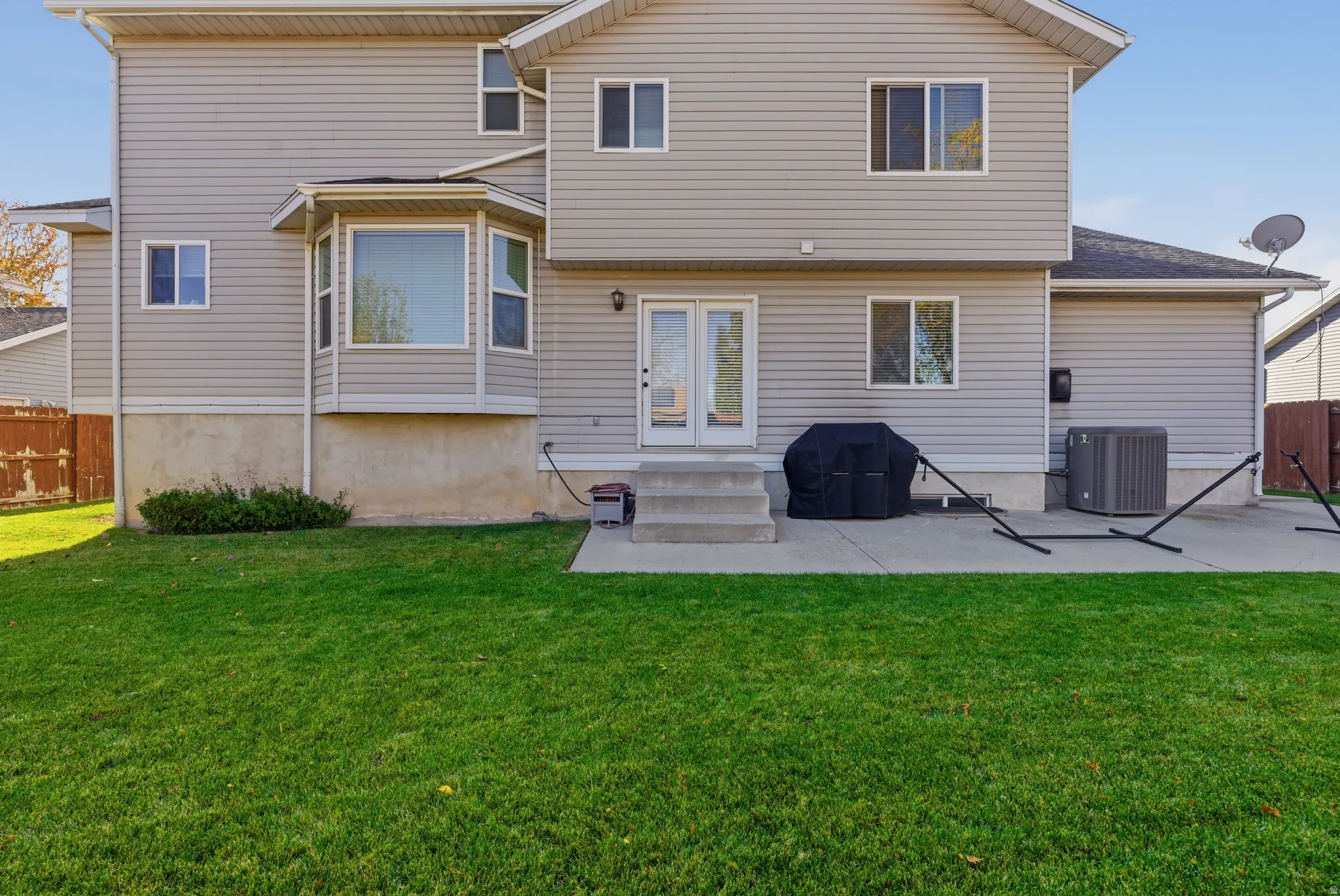 Rear exterior featuring light grey siding, a concrete patio, and a manicured lawn