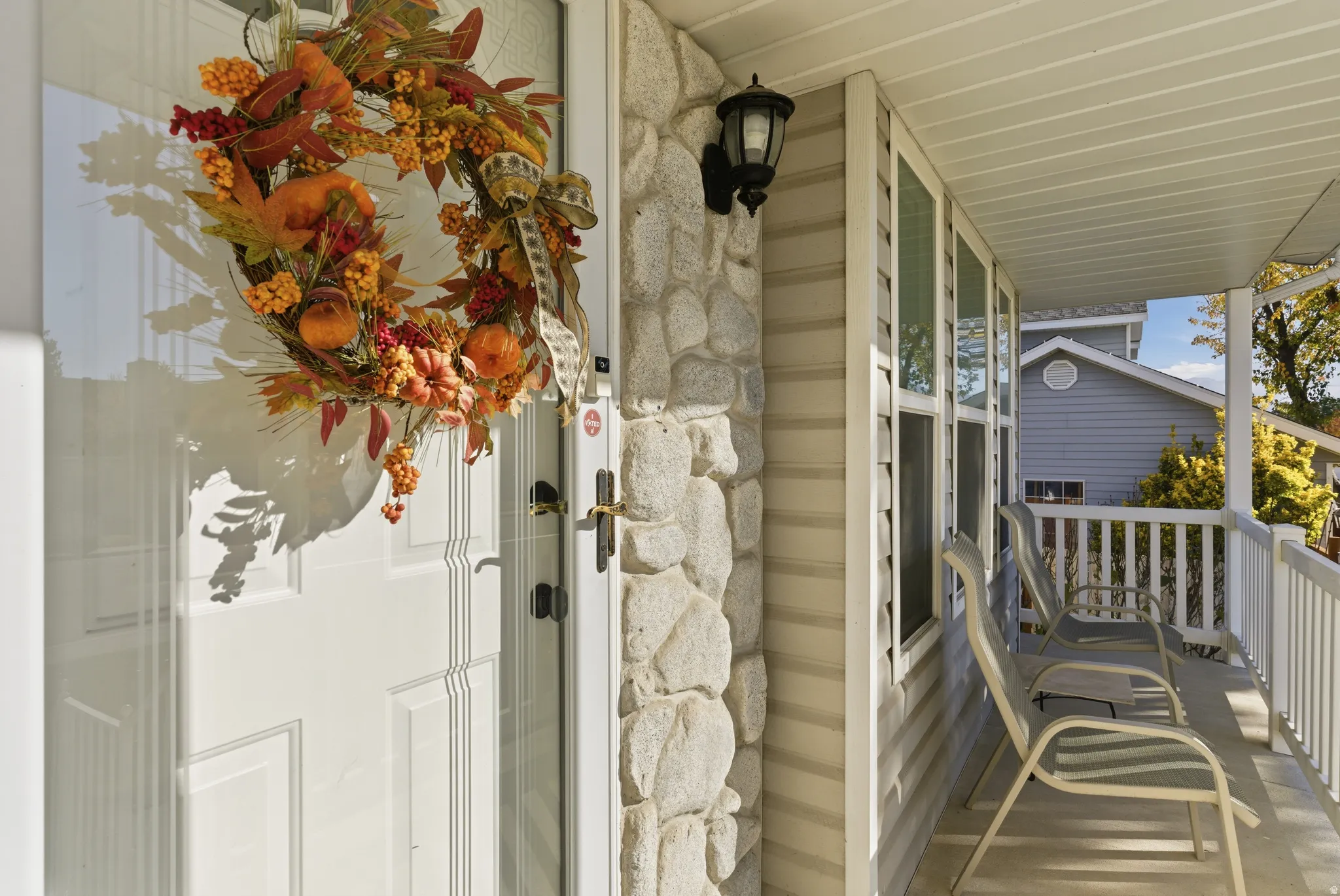 Covered front porch featuring a white entry door with glass storm door, stone veneer accent wall, and vinyl siding
