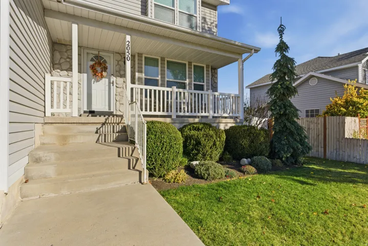 Inviting front porch with white railings, concrete steps, and stone accents