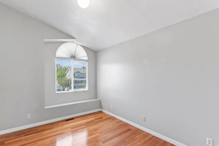 Room featuring wood-finish flooring, a vaulted ceiling, and a large arched window with horizontal blinds and a window ledge