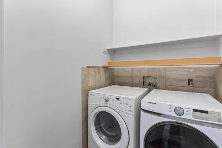 Dedicated laundry area featuring wall tiling, white walls, and a wall-mounted shelf