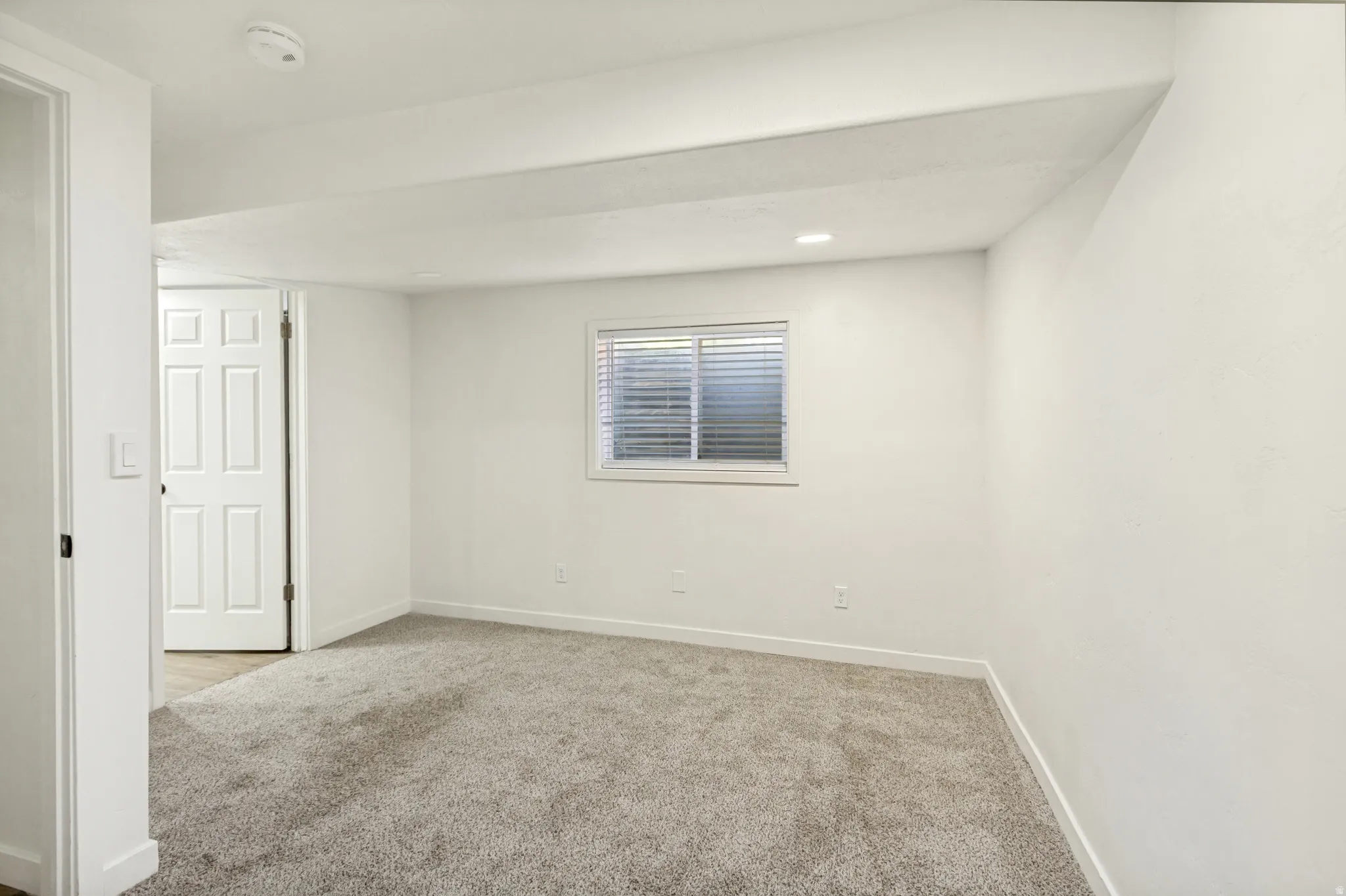 Bedroom featuring a neutral grey carpet, a white framed window with horizontal blinds, and recessed ceiling lighting