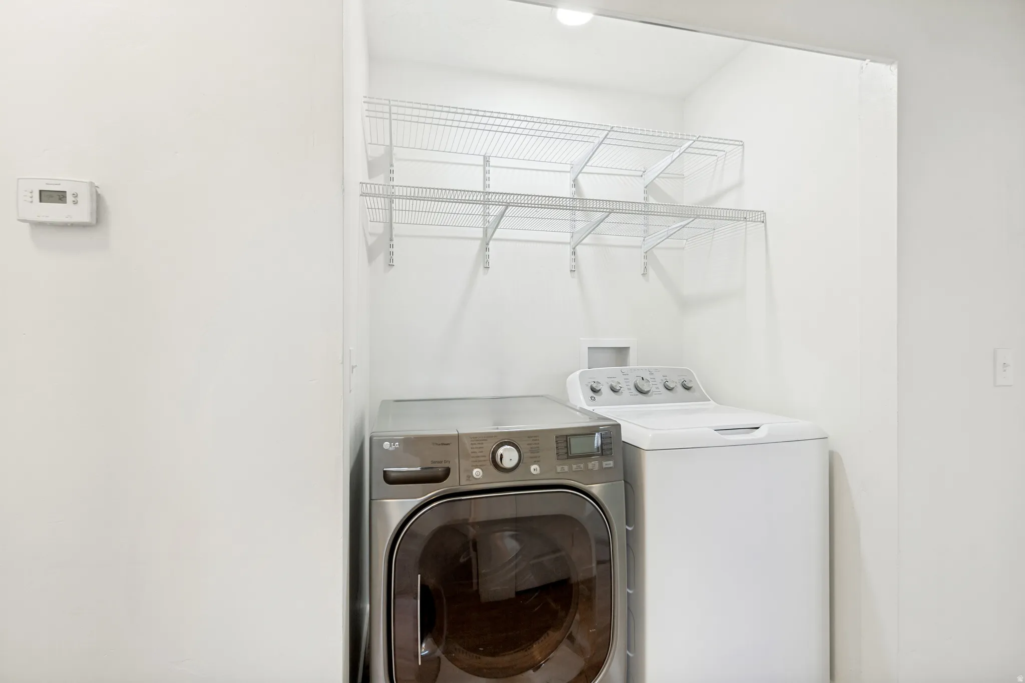 Dedicated laundry area featuring a front-load washer, top-load dryer, and wire shelving