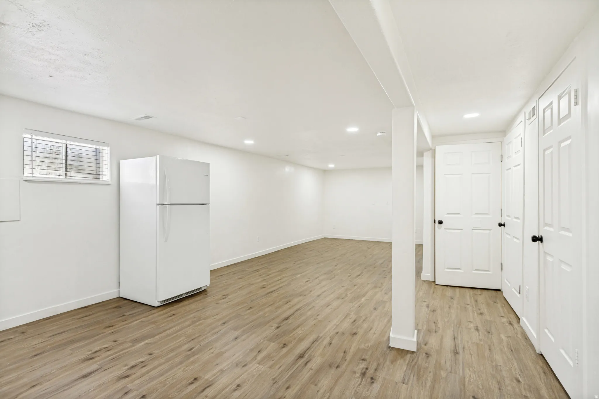 Spacious room featuring wood-finish flooring, recessed lighting, and bright white walls