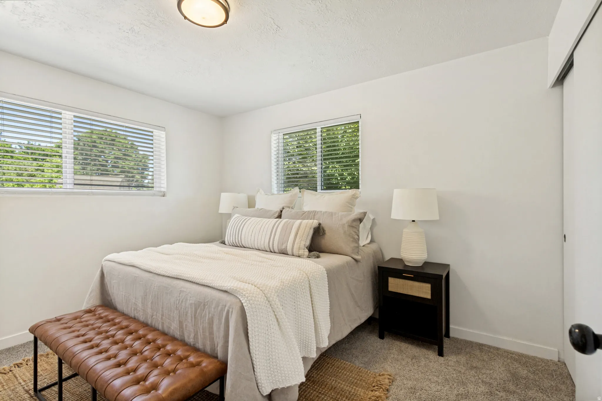 Carpeted bedroom featuring multiple windows with blinds, a ceiling-mounted light fixture, and a sliding closet door