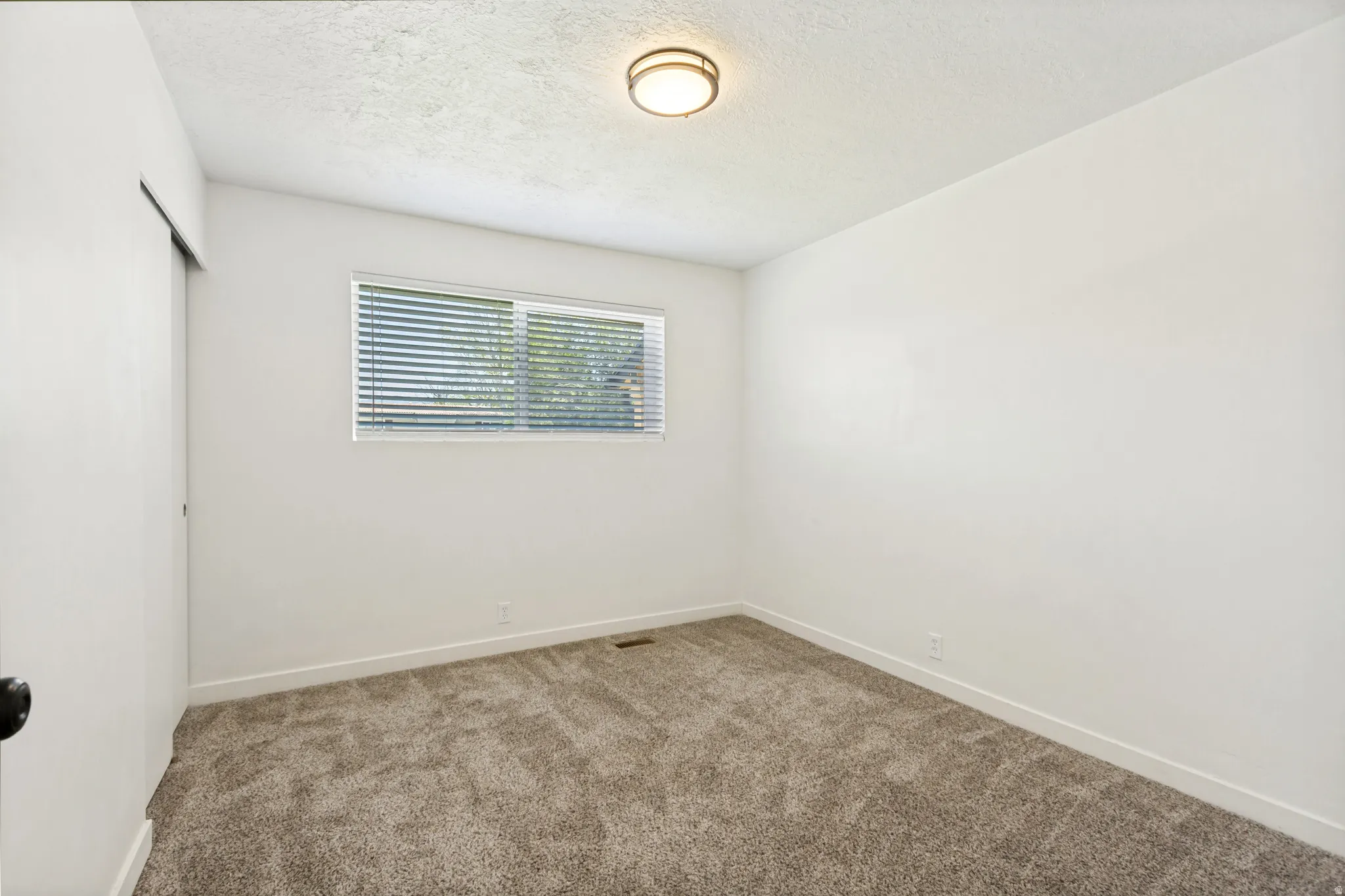 Carpeted room featuring a single window with horizontal blinds, a ceiling-mounted light fixture, and white painted walls