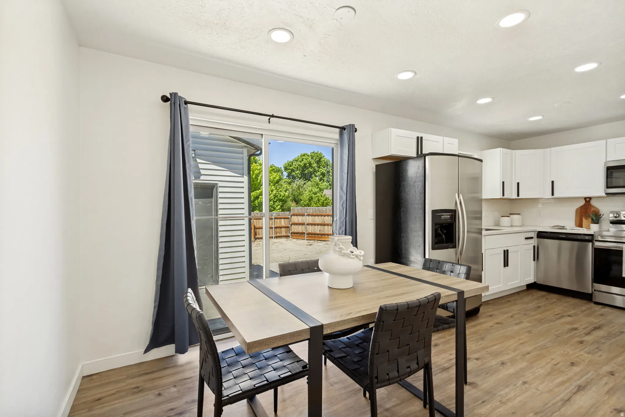 Open-concept kitchen featuring white cabinetry, stainless steel appliances, and wood-look flooring