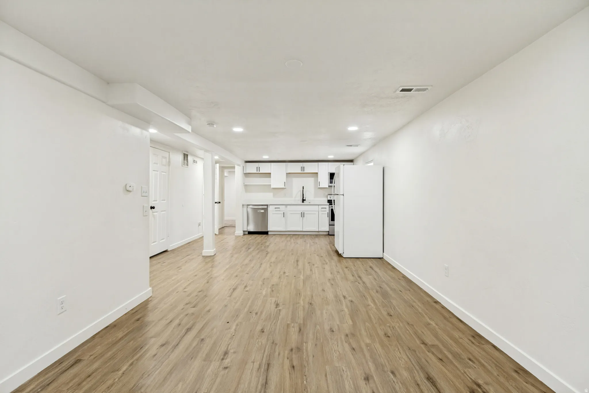 Open-concept living area featuring wood-finish flooring, recessed lighting, and a kitchen with white cabinetry, stainless steel appliances, and a black faucet