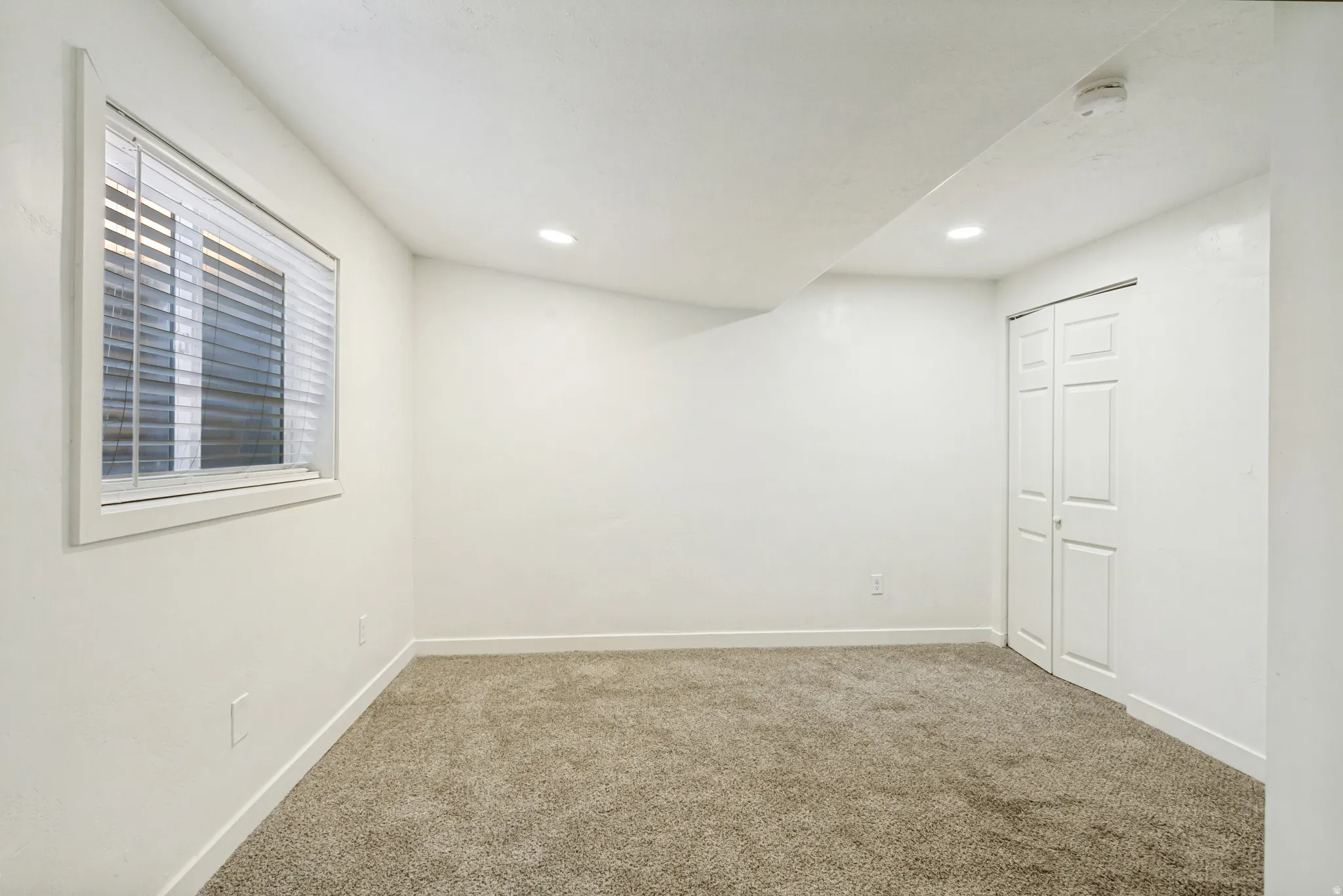 Carpeted bedroom featuring a window with horizontal blinds, bi-fold closet doors, recessed lighting, and white baseboards