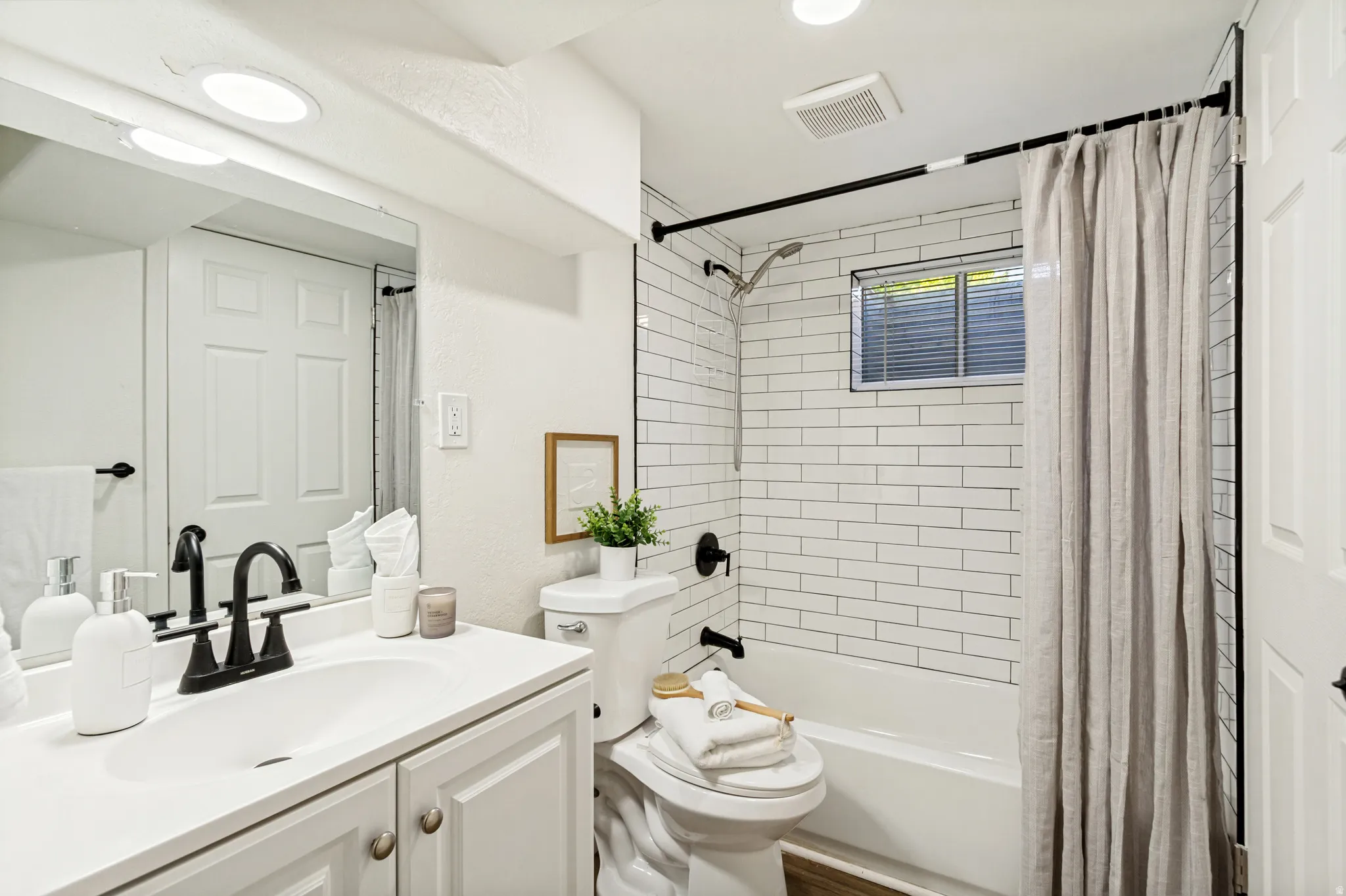 Bathroom featuring a white vanity with integrated sink, matte black faucet, and a subway-tiled shower with a tub