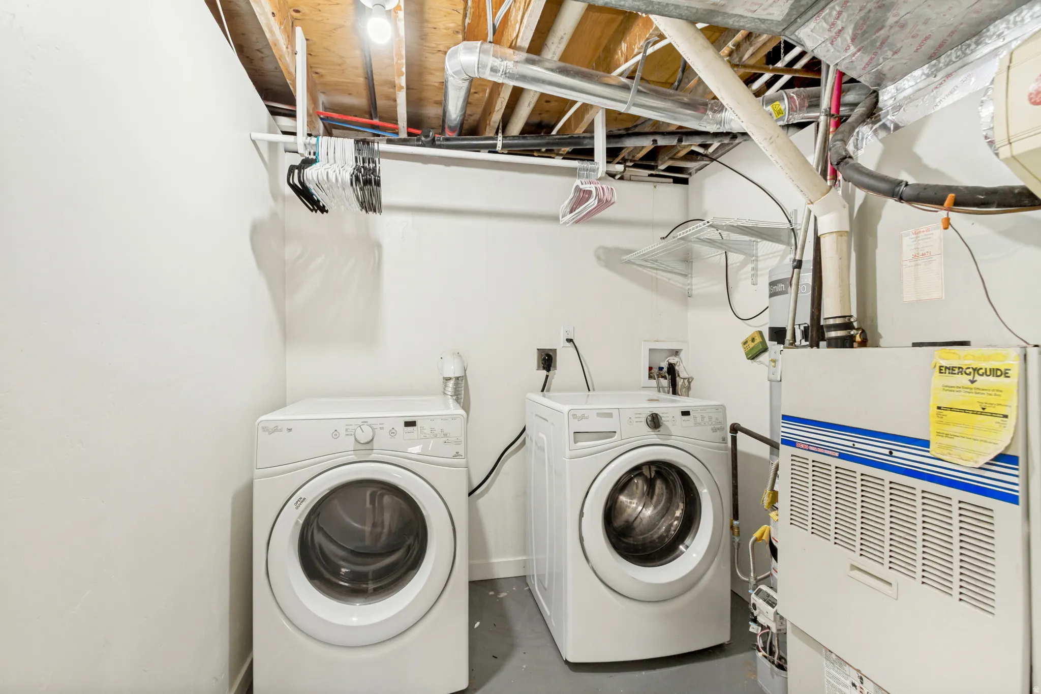 Dedicated laundry area featuring a white front-load washing machine and dryer, a utility sink, overhead lighting, and an exposed ceiling with visible ductwork