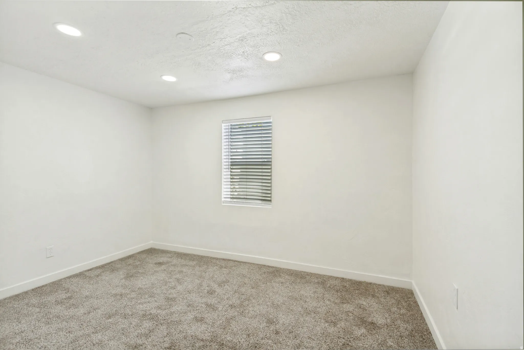 Neutral color palette throughout featuring recessed lighting, a single window with blinds, and low-pile carpet