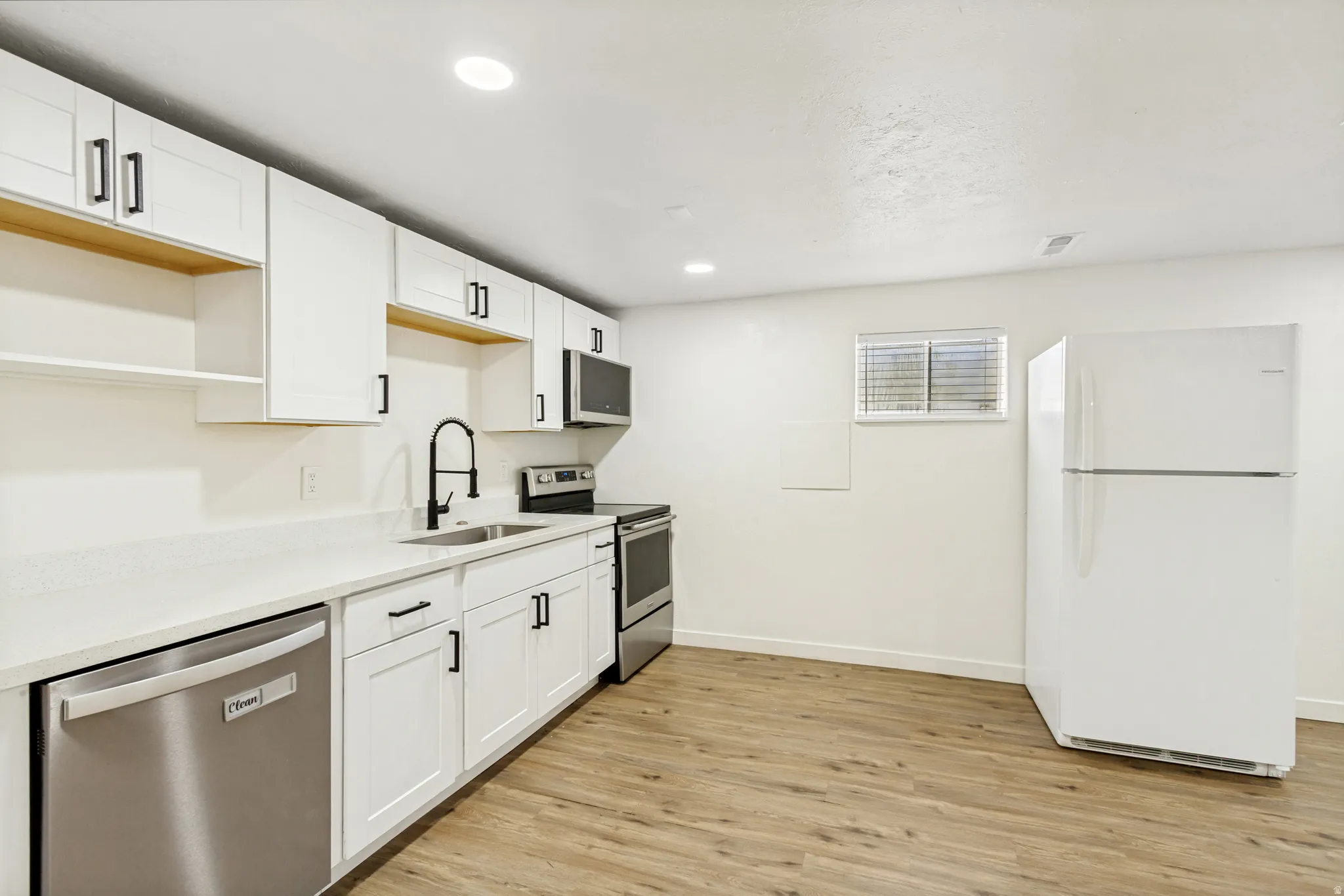 Updated kitchen featuring white shaker cabinetry, quartz countertops, a matte black faucet, stainless steel appliances, and wood-look flooring
