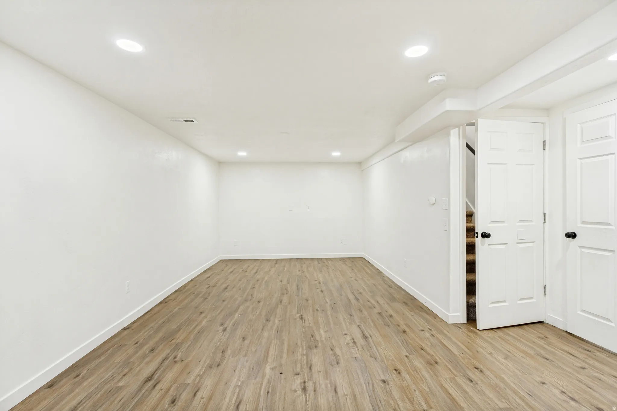 Spacious room featuring wood-finish flooring, white walls, recessed ceiling lighting, and white trim