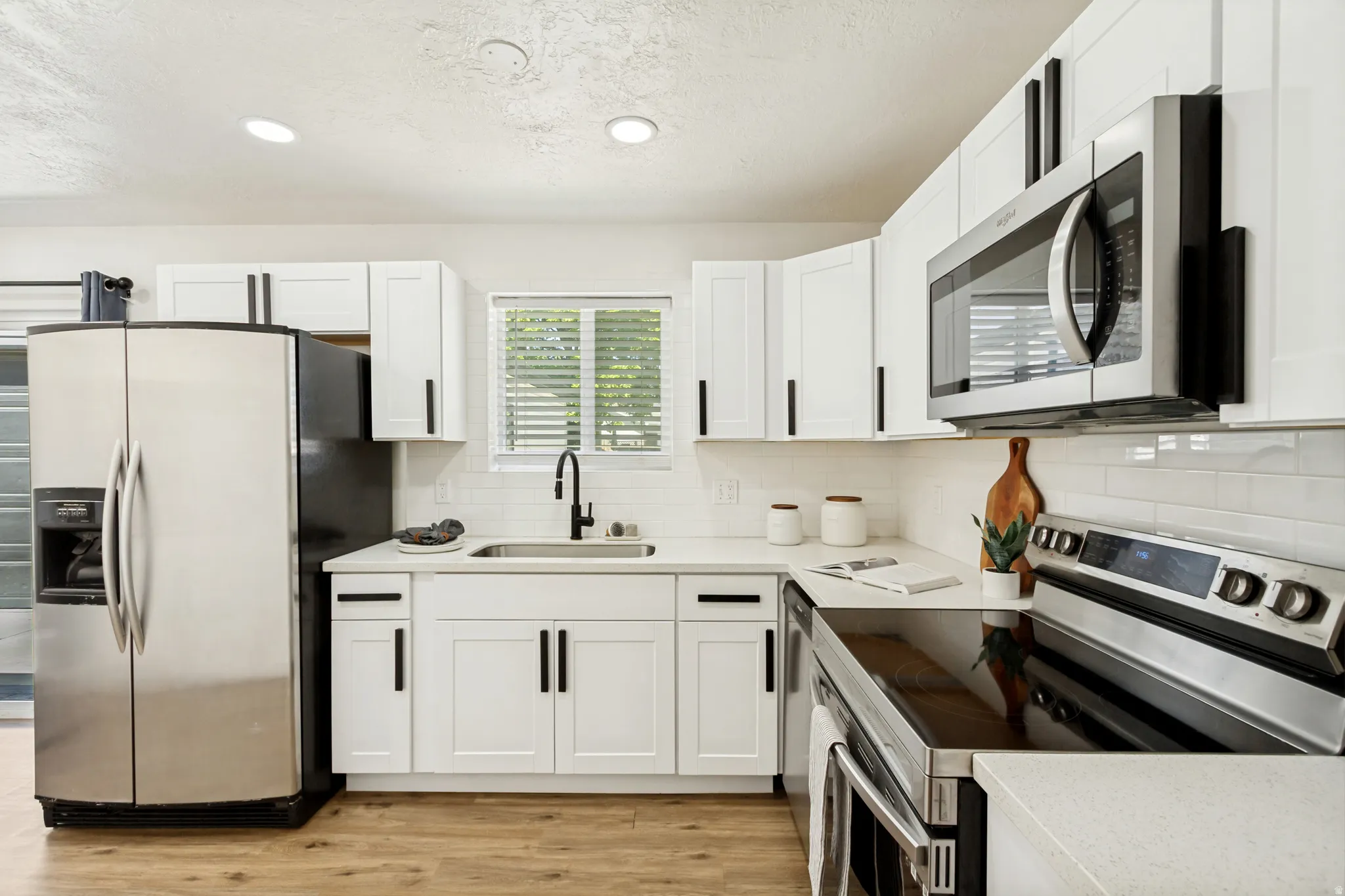 Bright kitchen featuring white shaker cabinetry, stainless steel appliances, a subway tile backsplash, and wood-finish flooring