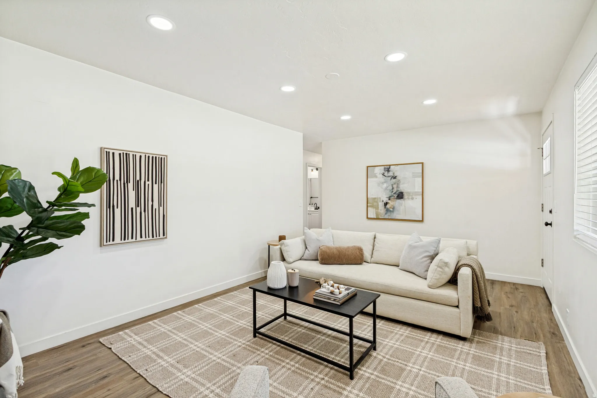 Bright living area featuring recessed lighting, wood-finish flooring, white baseboards, and a white entry door with a frosted glass panel