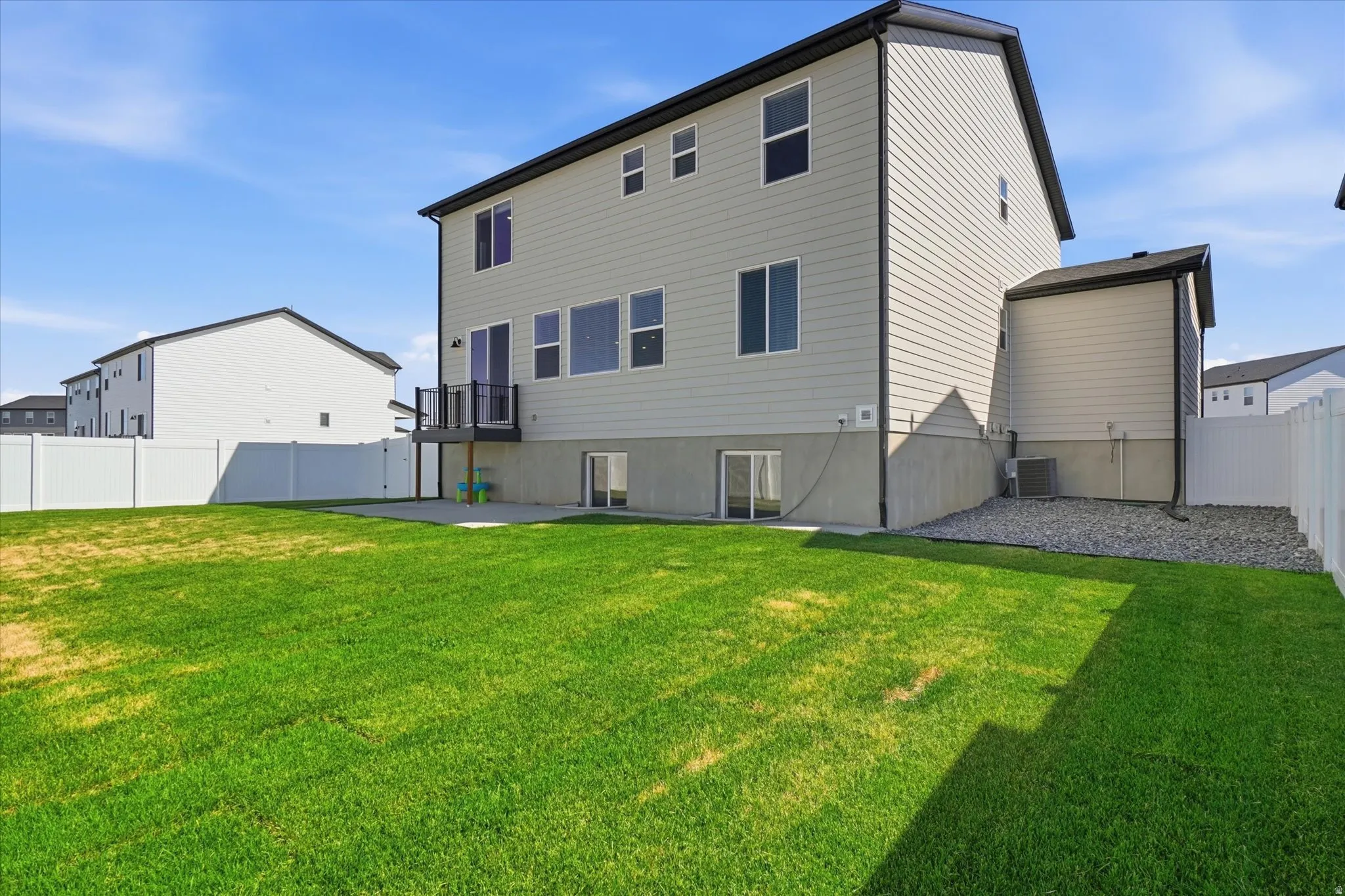 Expansive rear yard featuring green lawn, a white privacy fence, a concrete patio, and a second-story deck with dark railings