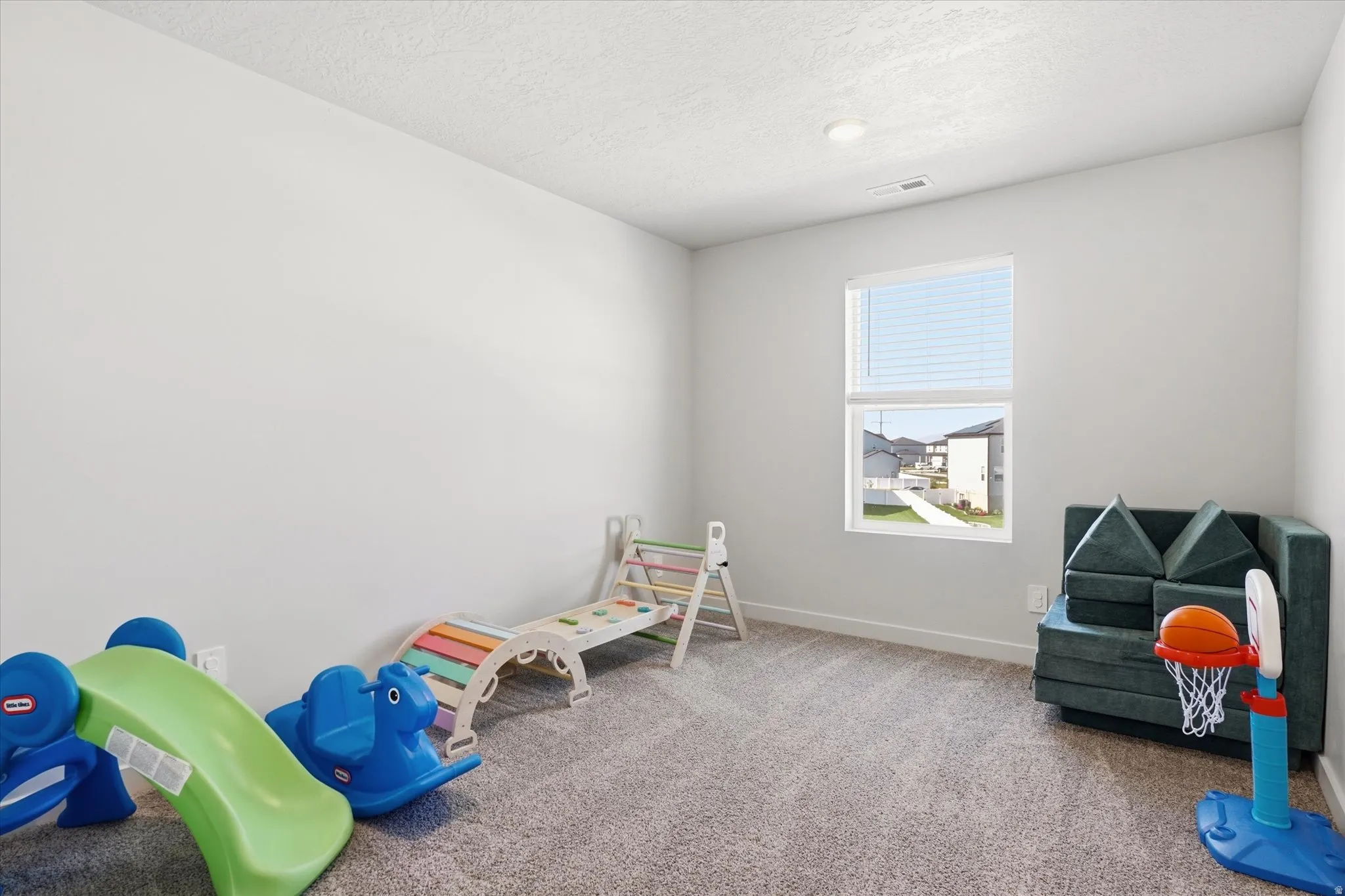 Carpeted room with a single window featuring blinds, a ceiling light fixture, and white painted walls