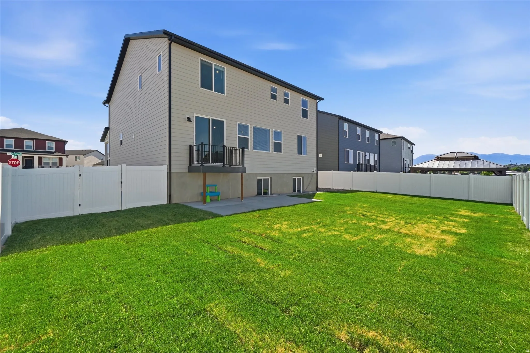 Expansive backyard featuring a lush lawn, white vinyl fencing, and a concrete patio
