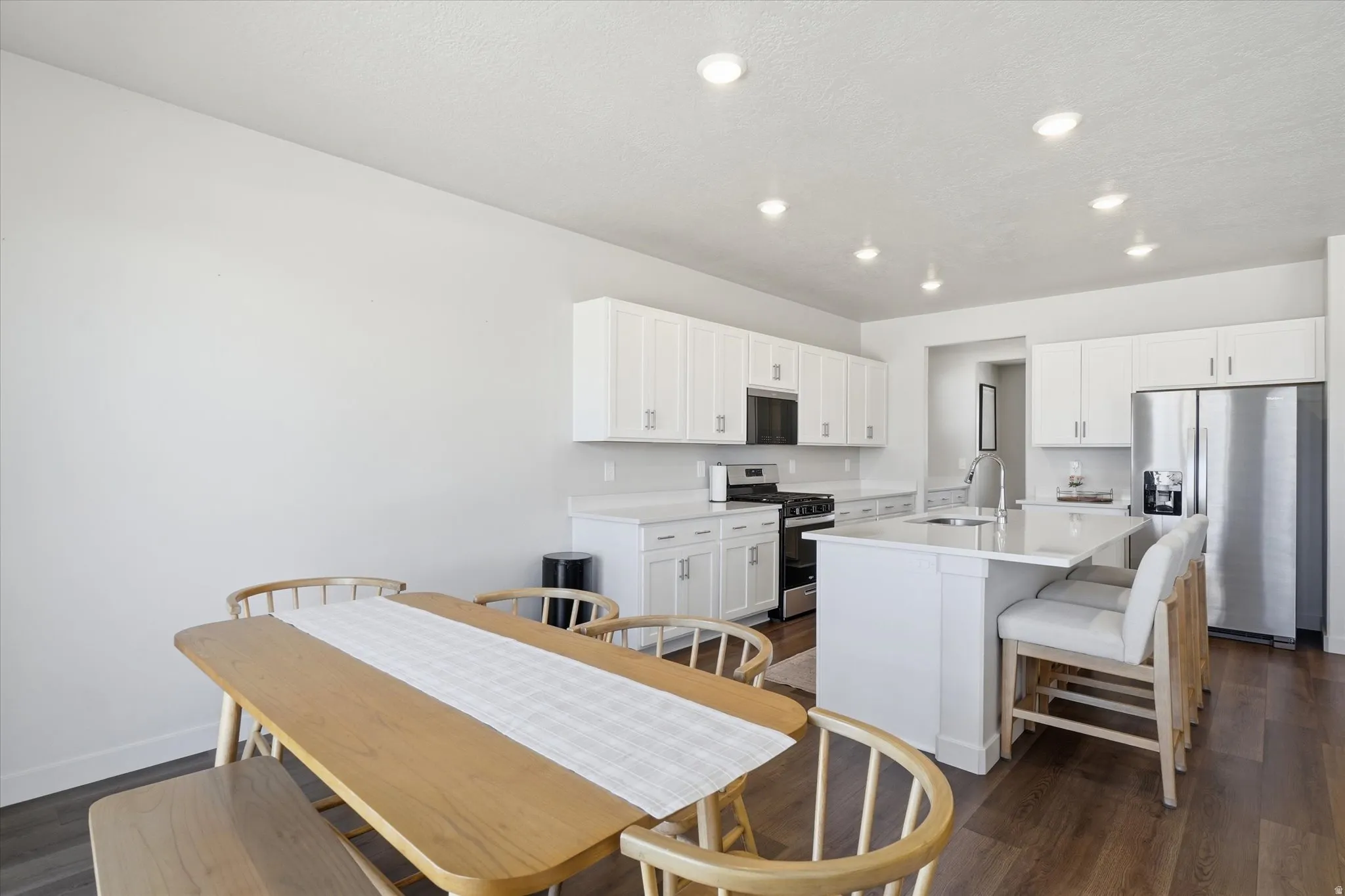 Modern kitchen featuring bright white cabinetry, stainless steel appliances, a center island with seating, recessed lighting, and wood-finish flooring