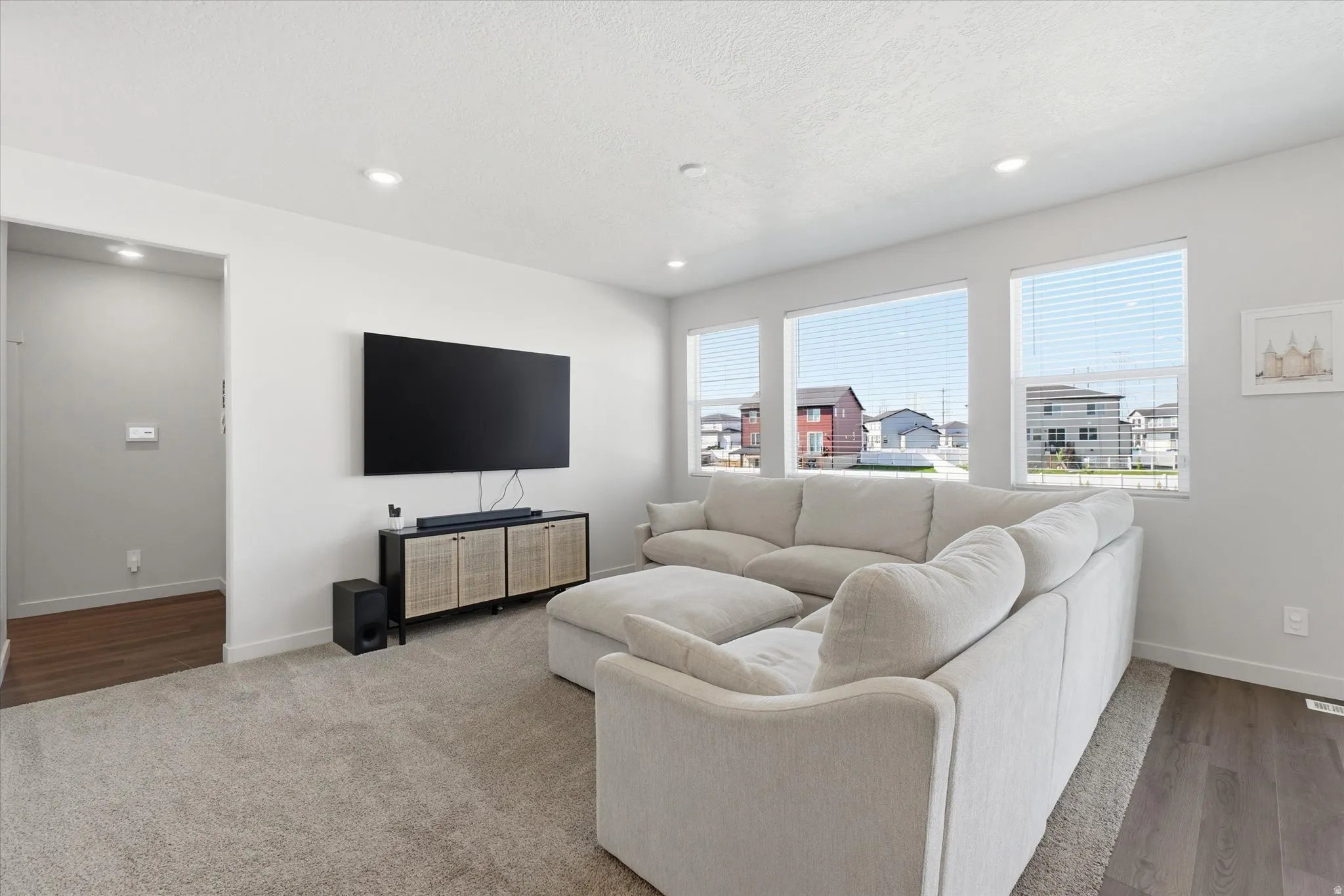 Bright living area featuring recessed lighting, a wide window line with blinds, a wall-mounted display, and a built-in media console