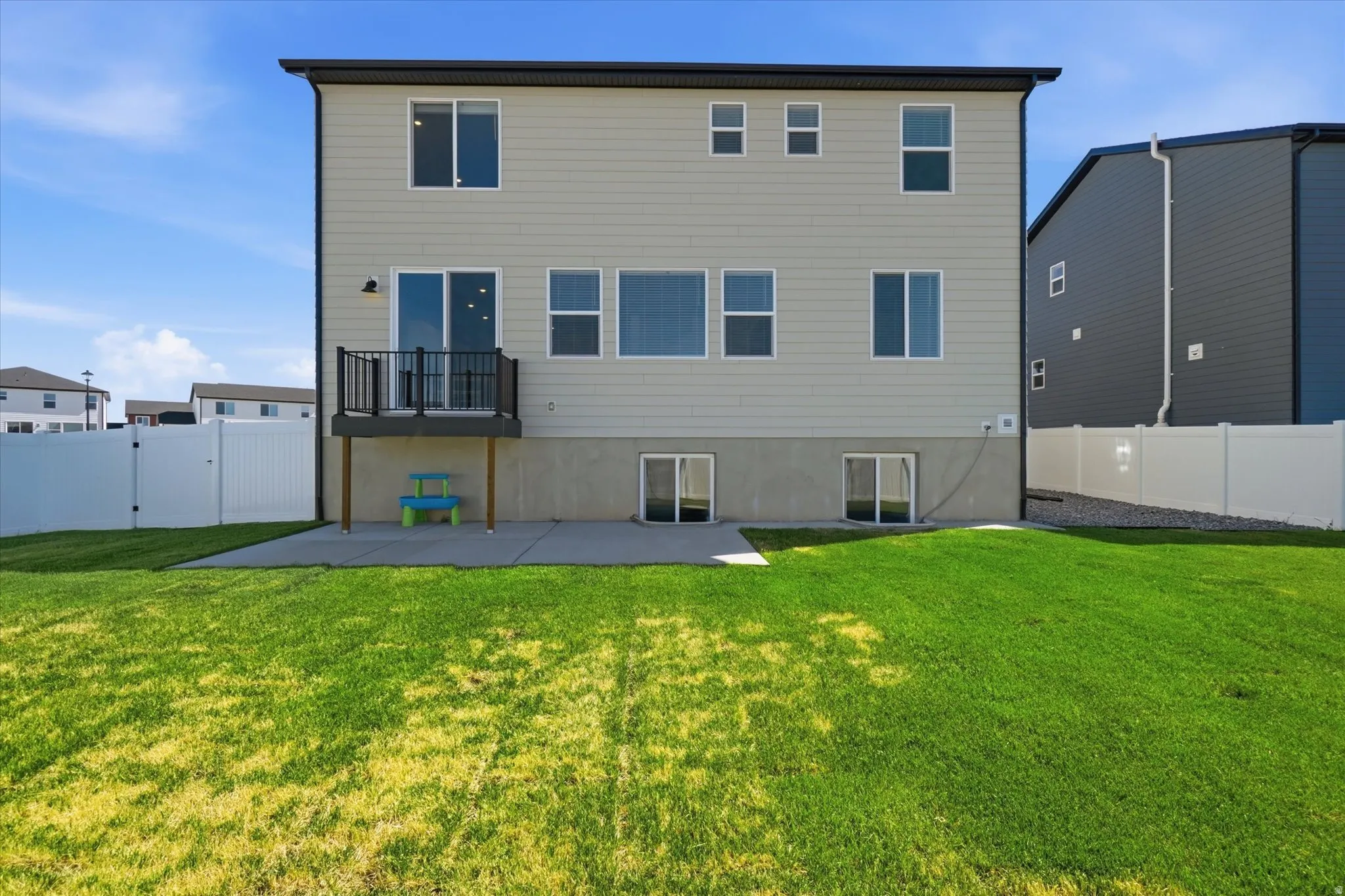 Rear exterior featuring neutral-toned siding, a second-story deck with dark railings, and a concrete patio