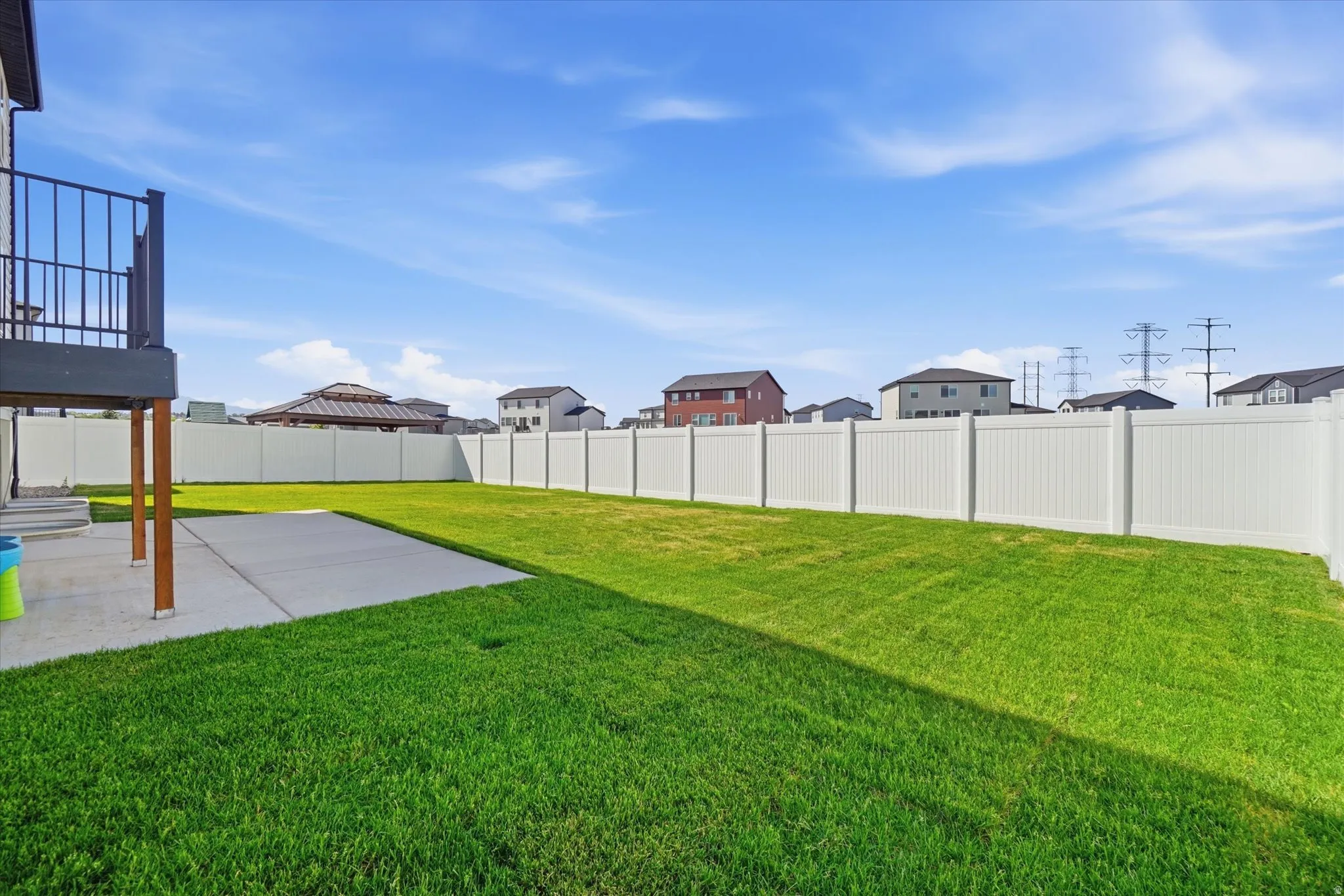 Expansive backyard featuring a lush green lawn, full vinyl fencing, and a concrete patio