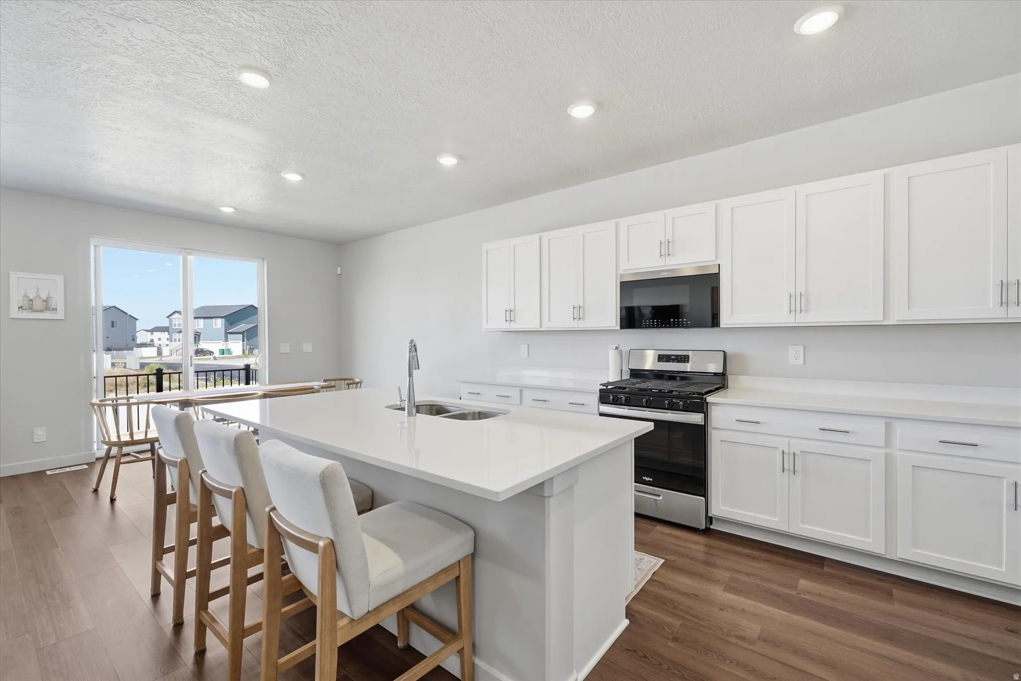 Kitchen featuring a spacious island with an undermount sink, white cabinetry, stainless steel appliances, and wood-finish flooring
