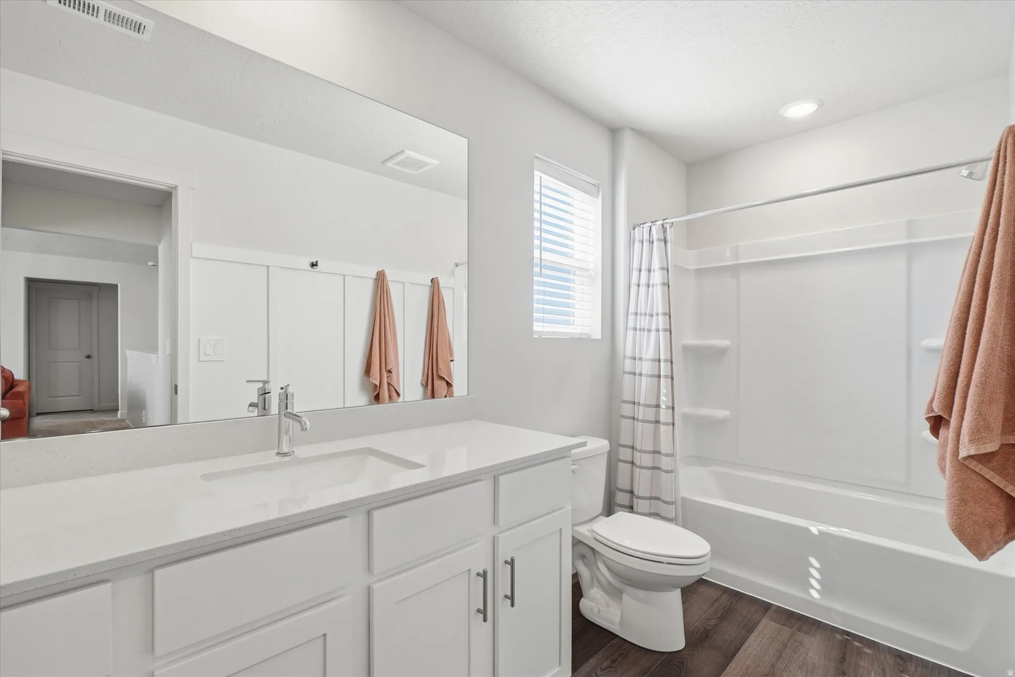 Contemporary bathroom featuring a white vanity with an integrated sink and chrome faucet, a large frameless mirror, a white bathtub with an integrated shower, and dark wood-finish flooring