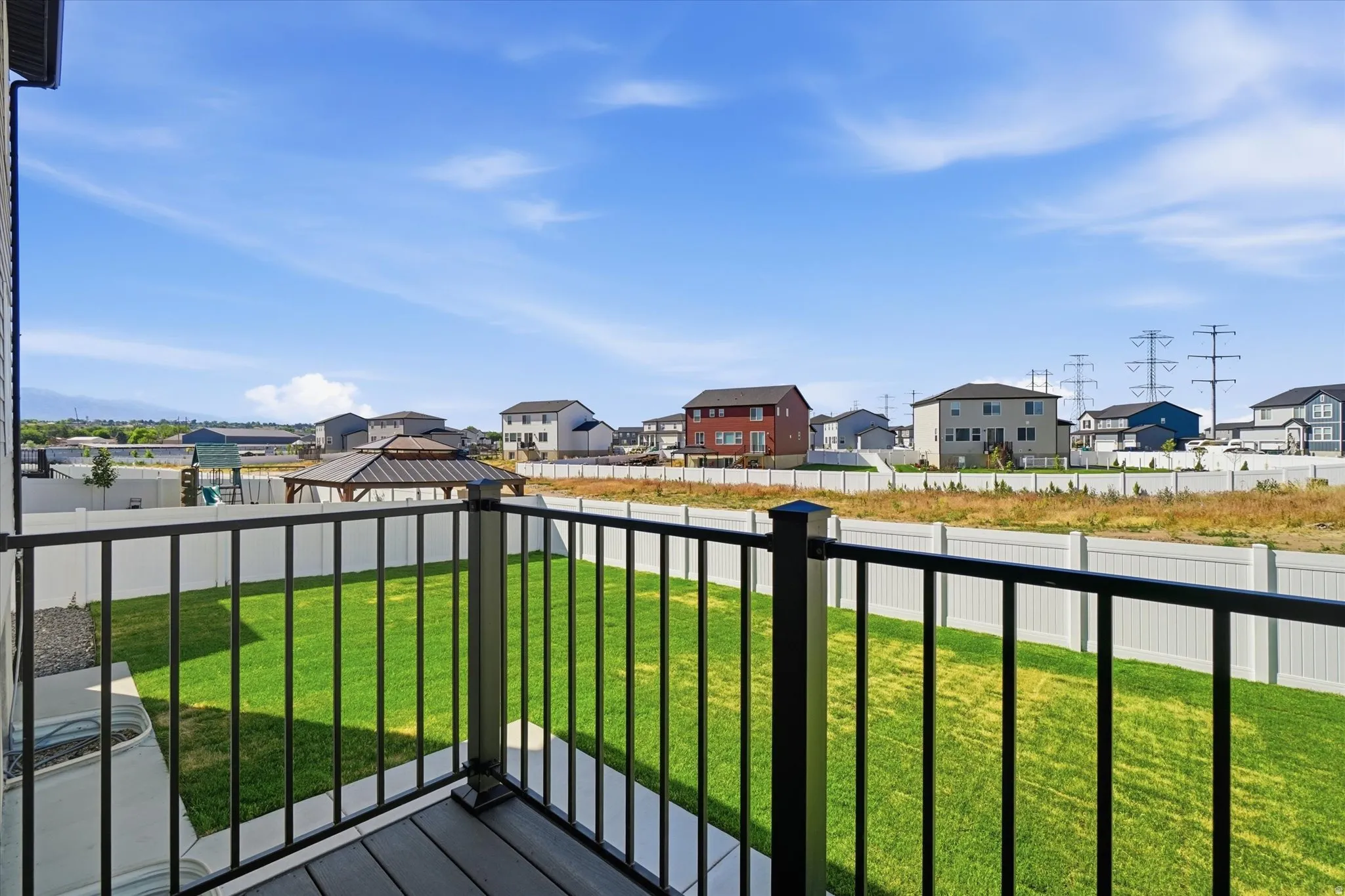Outdoor deck with dark composite flooring and black metal railings overlooks a grassy backyard