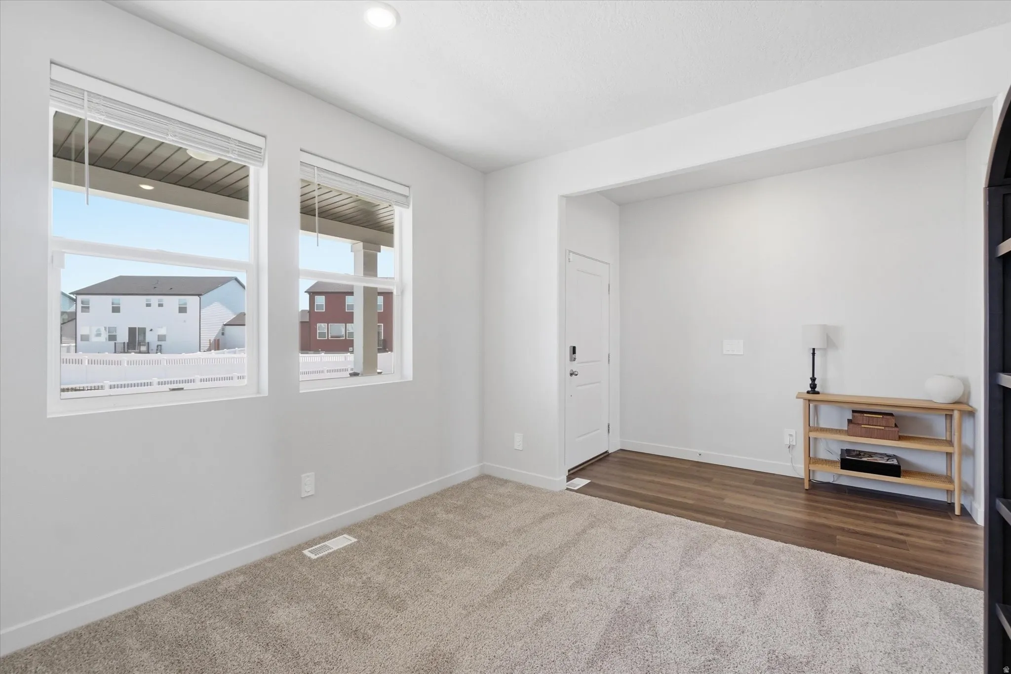 Bright interior space featuring two large windows, neutral carpeting, and wood-finish flooring