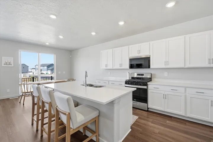 Kitchen featuring a spacious island with an undermount sink, white cabinetry, stainless steel appliances, and wood-finish flooring