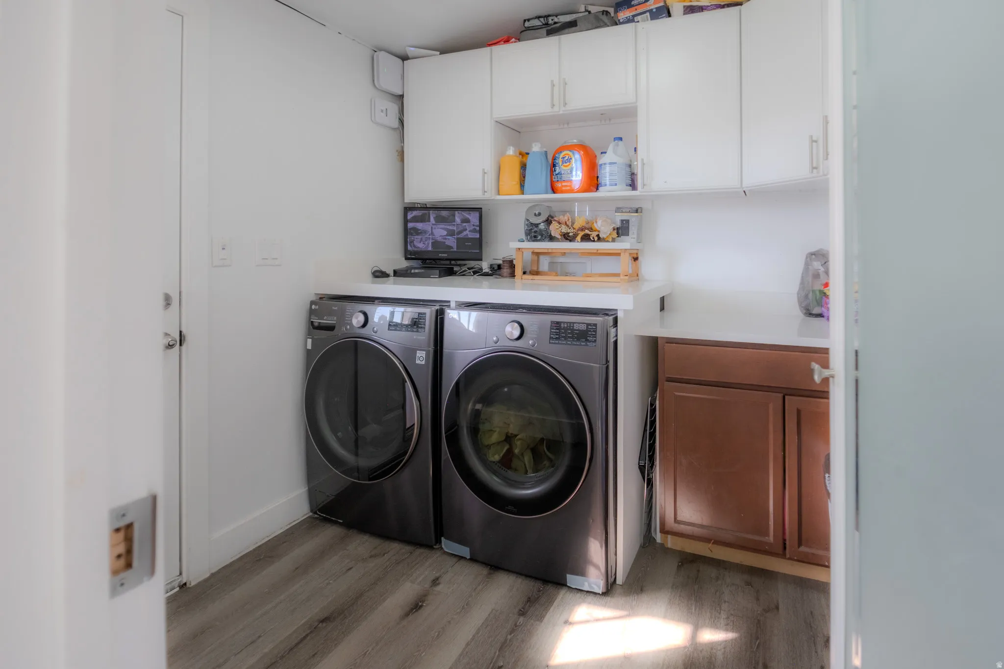 Dedicated laundry area featuring front-loading appliances, white cabinetry, integrated countertop space, wood-finish flooring, and a built-in base cabinet with a brown finish