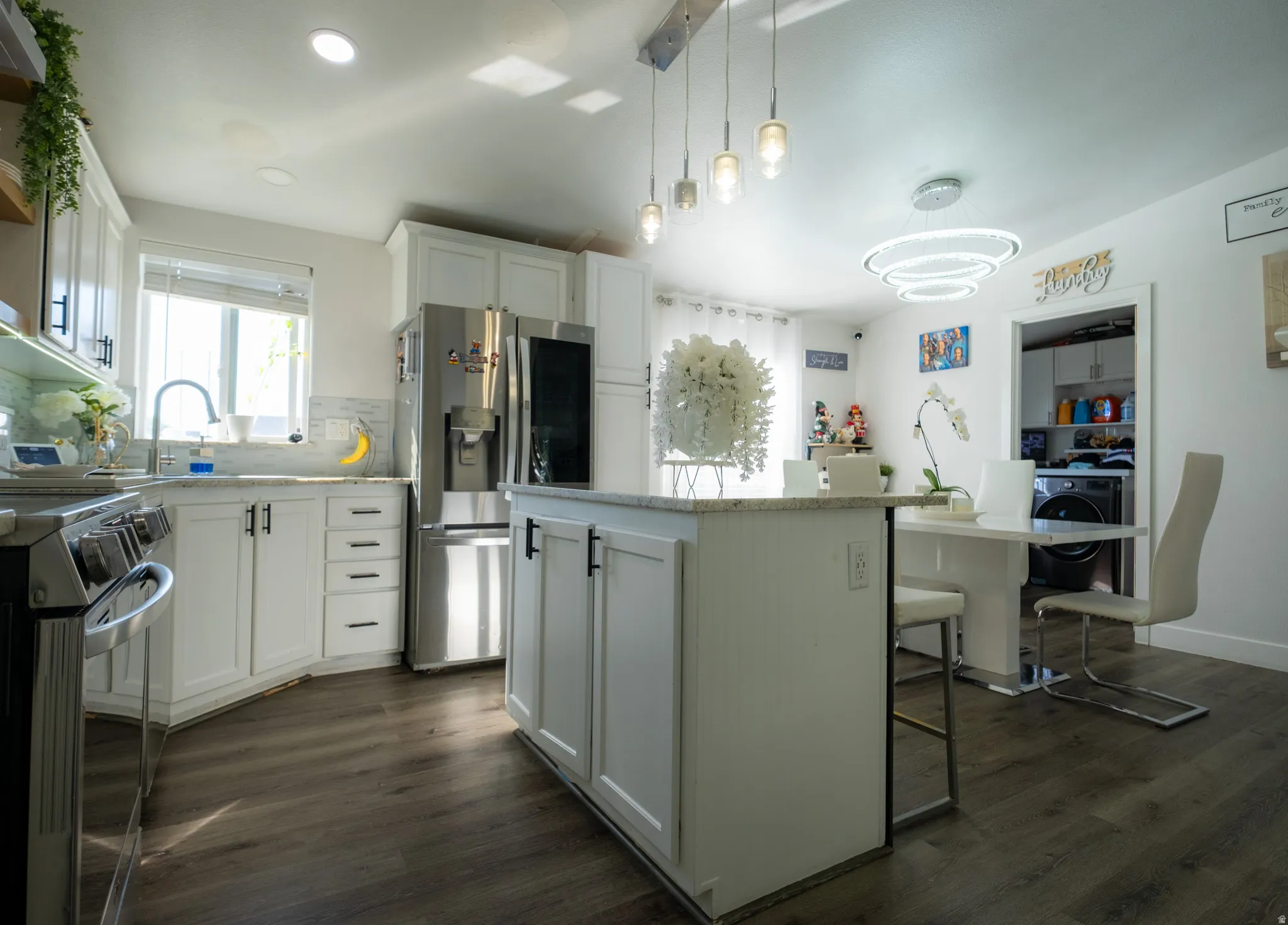 Modern kitchen featuring white shaker cabinetry with dark hardware, stainless steel appliances, a center island with a granite-style countertop, and wood-finish flooring