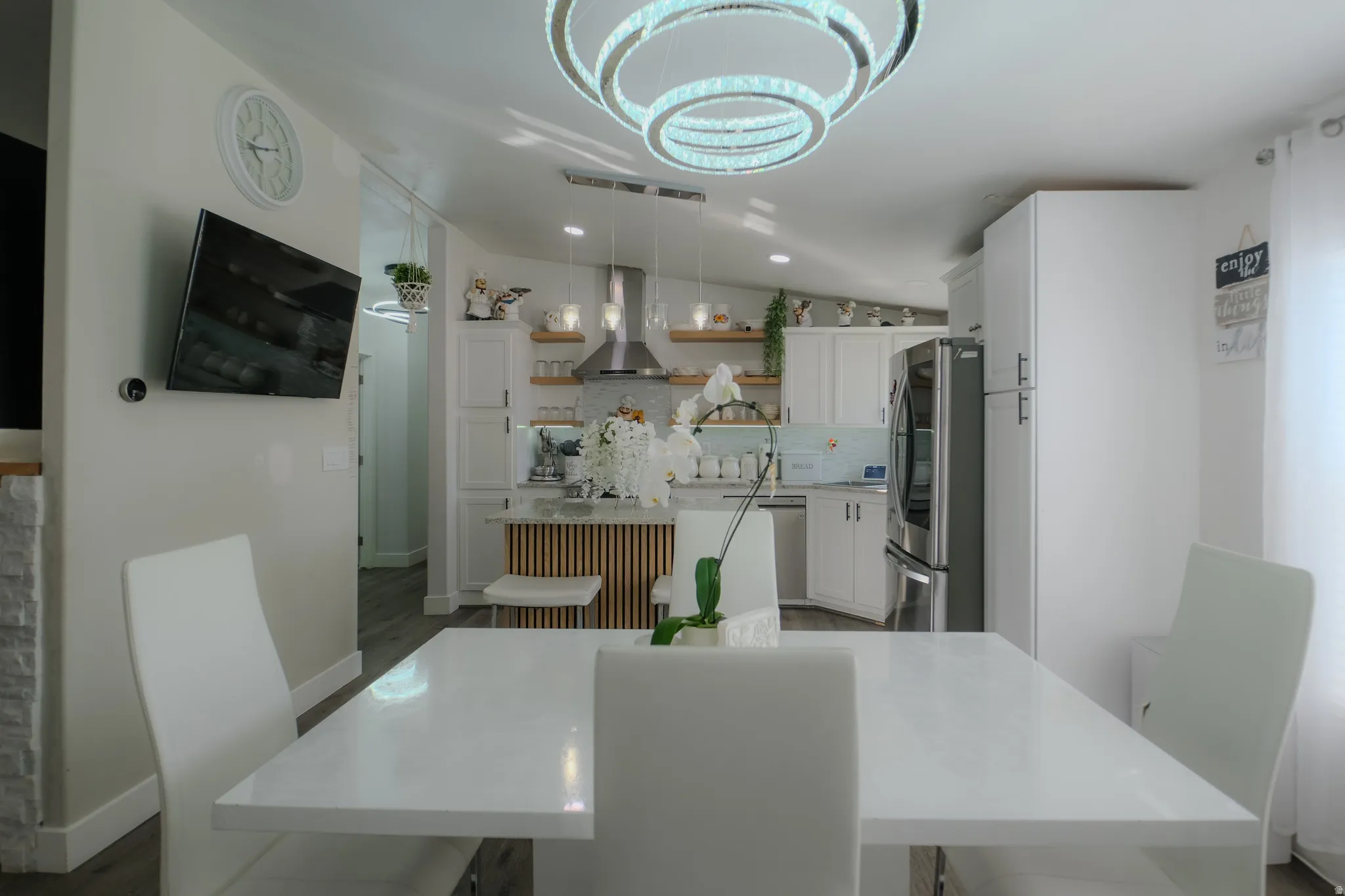 Open-concept dining and kitchen space featuring a modern ring chandelier, white dining table, and light wood-finish flooring