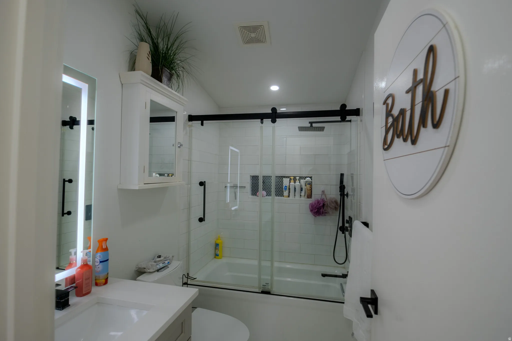 Modern bathroom featuring a tiled tub/shower combination with a sliding glass door and matte black hardware