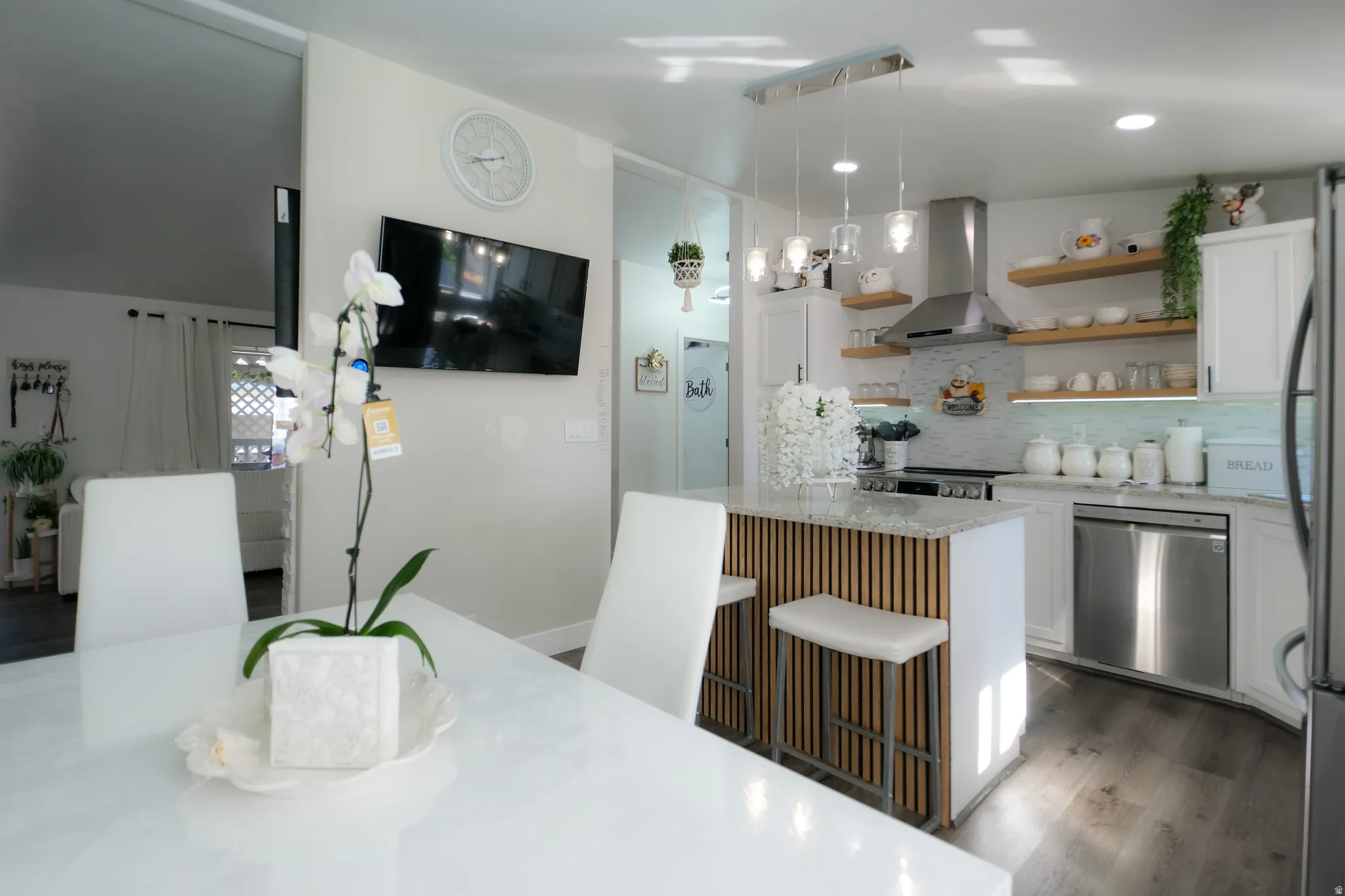 Kitchen featuring white cabinetry, light wood open shelving, a stainless steel range hood, stainless steel appliances, and a kitchen island with a slatted wood-finish base and light-colored countertop