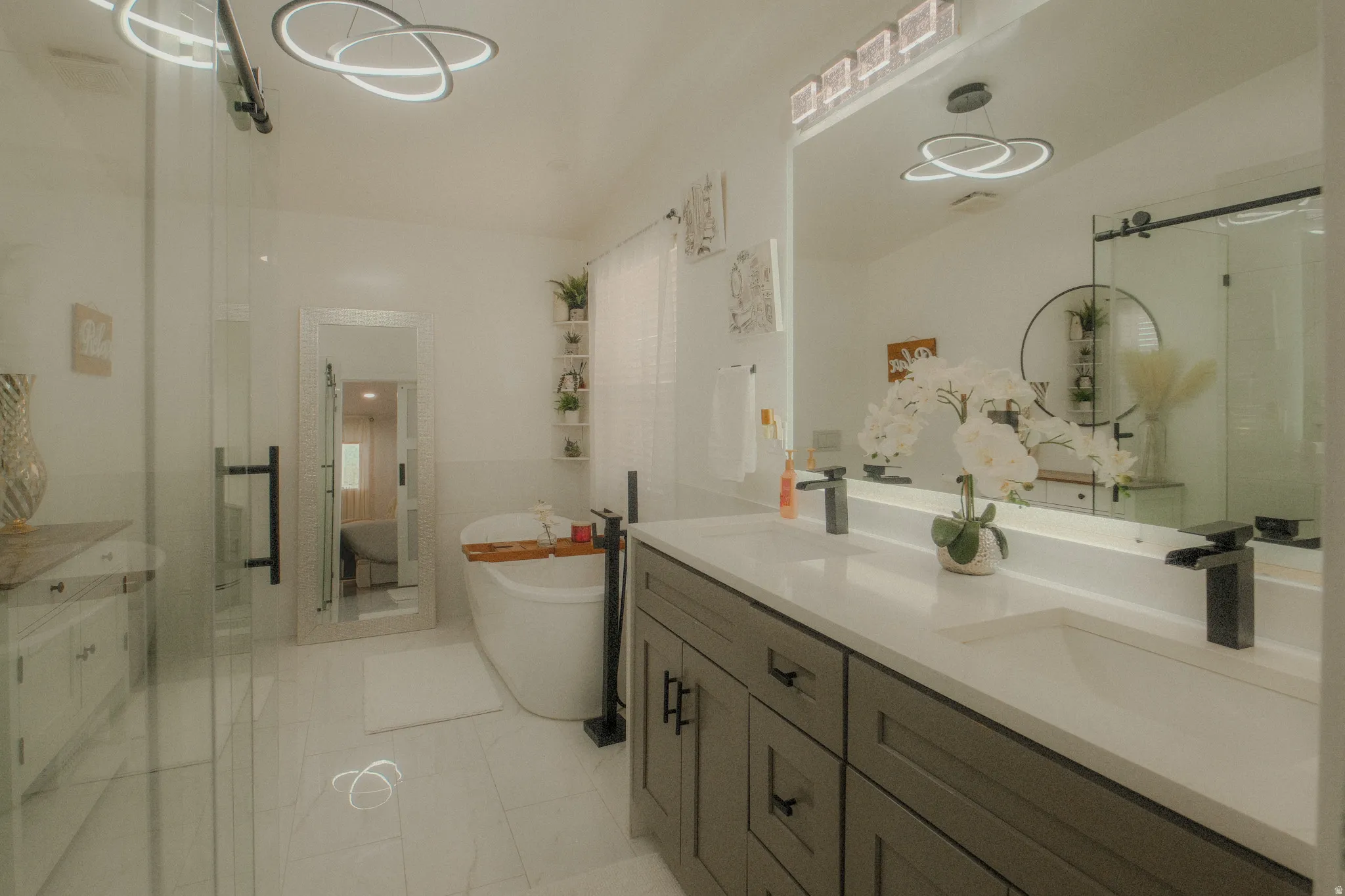 Contemporary bathroom featuring a freestanding soaking tub with floor-mounted fixtures, a dual vanity with undermount sinks and black matte faucets, and a glass-enclosed shower with a barn-door style entry