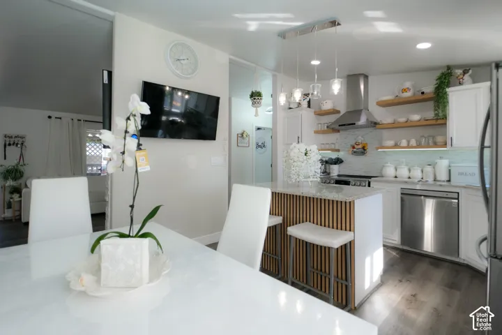 Kitchen featuring white cabinetry, light wood open shelving, a stainless steel range hood, stainless steel appliances, and a kitchen island with a slatted wood-finish base and light-colored countertop