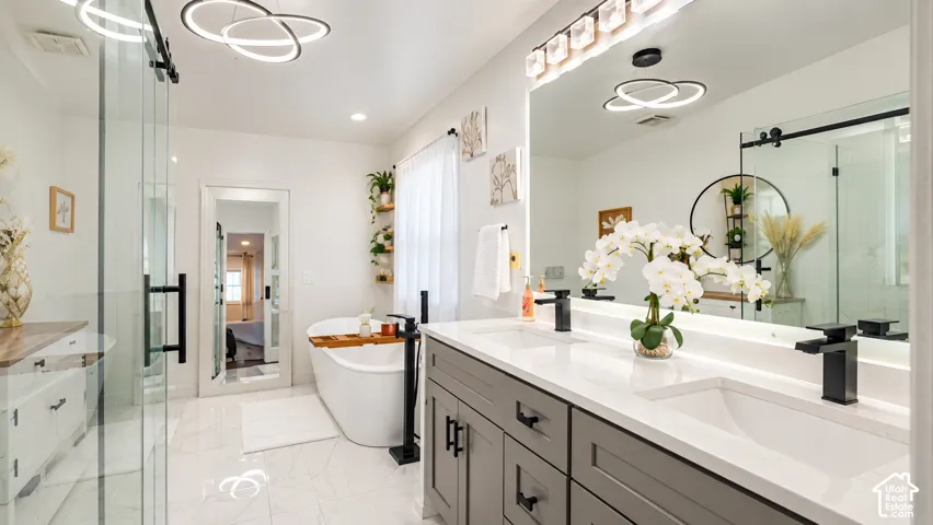Dual-sink vanity with quartz countertops and matte black fixtures, soaking tub, glass-enclosed shower, and decorative light fixtures