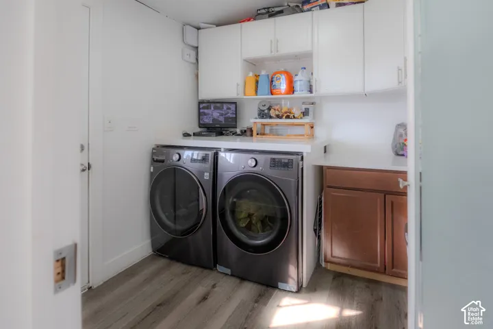 Dedicated laundry area featuring front-loading appliances, white cabinetry, integrated countertop space, wood-finish flooring, and a built-in base cabinet with a brown finish