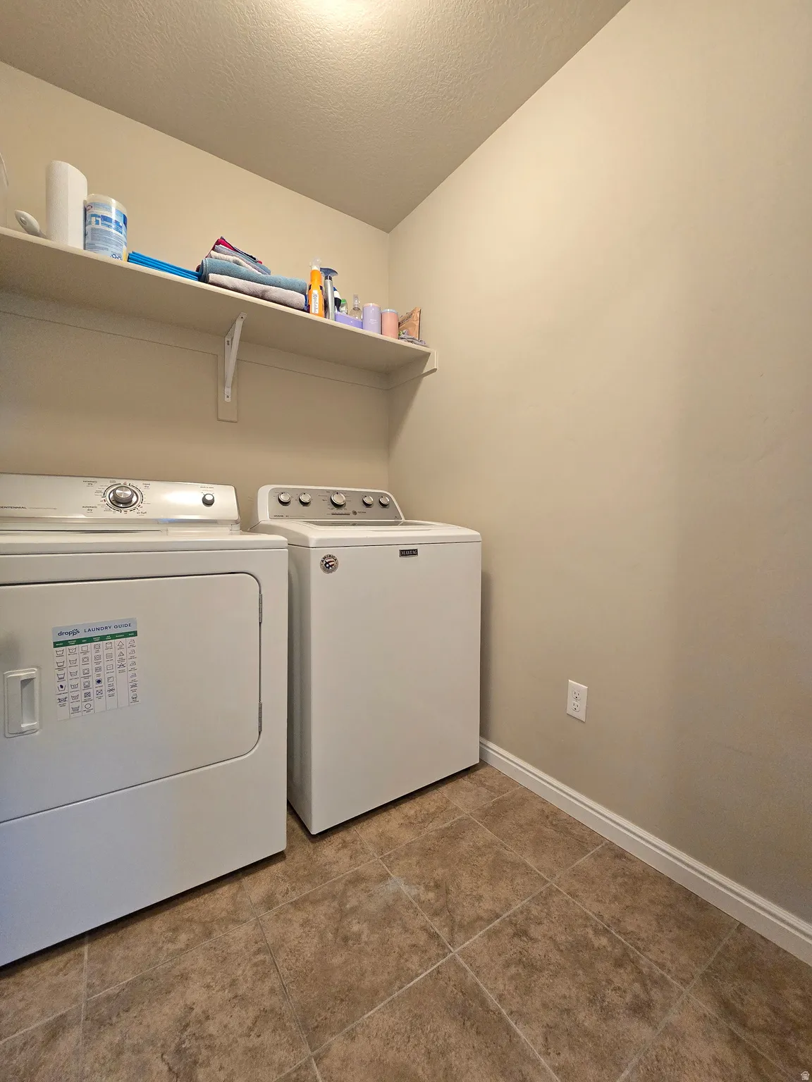 Dedicated laundry space featuring neutral wall paint, overhead shelving, and tile flooring