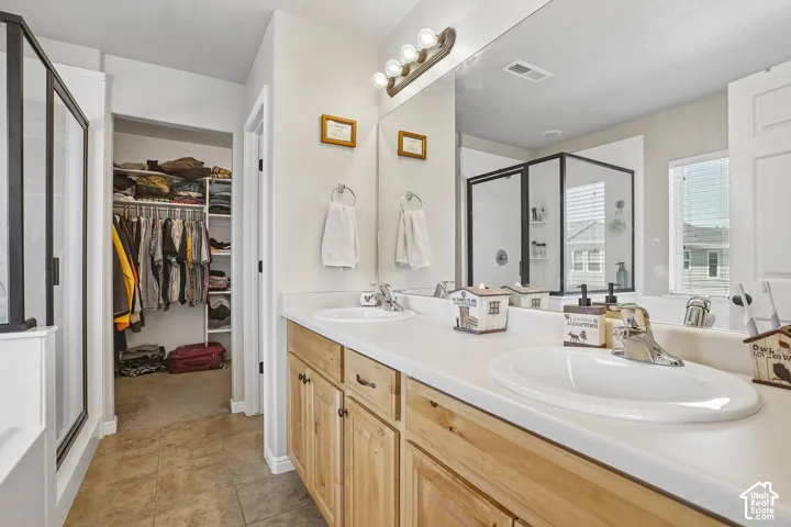 Double vanity with light wood cabinetry and integrated sinks, complemented by a large mirror and overhead four-bulb light fixture