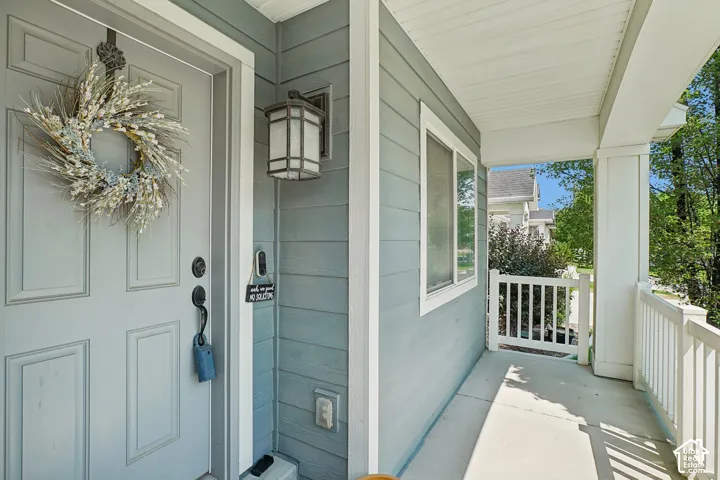 Covered front porch featuring a paneled entry door, horizontal siding, exterior sconce lighting, white trim, and a white railing