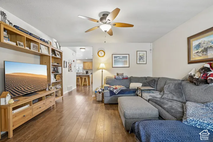 Living area featuring wood-finish flooring, a ceiling fan with light fixture, light neutral wall paint, and built-in shelving with cabinetry