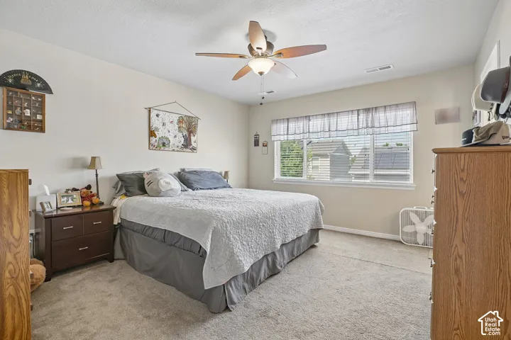 Spacious room featuring neutral wall tones, textured carpet flooring, a ceiling fan with integrated lighting, and a large window with horizontal blinds